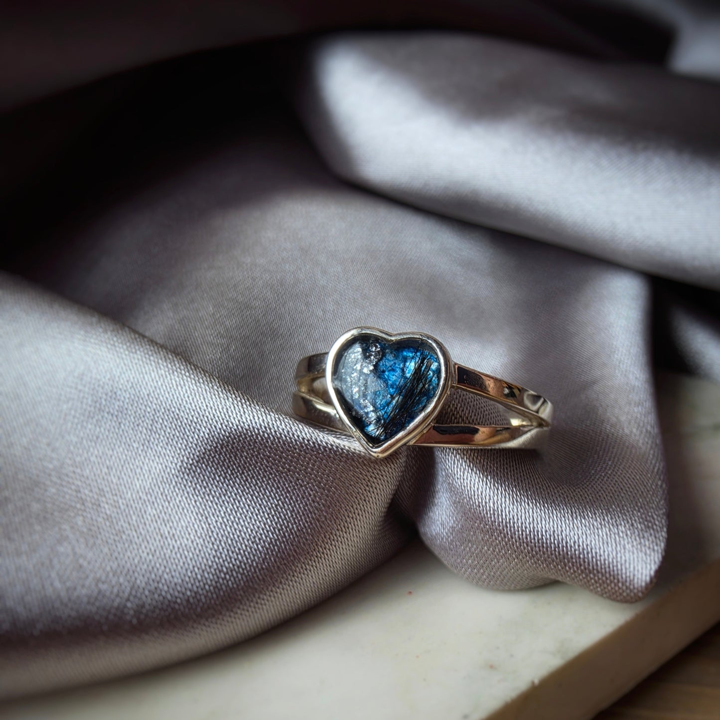 Heart-shaped blue gemstone ring on a textured fabric surface