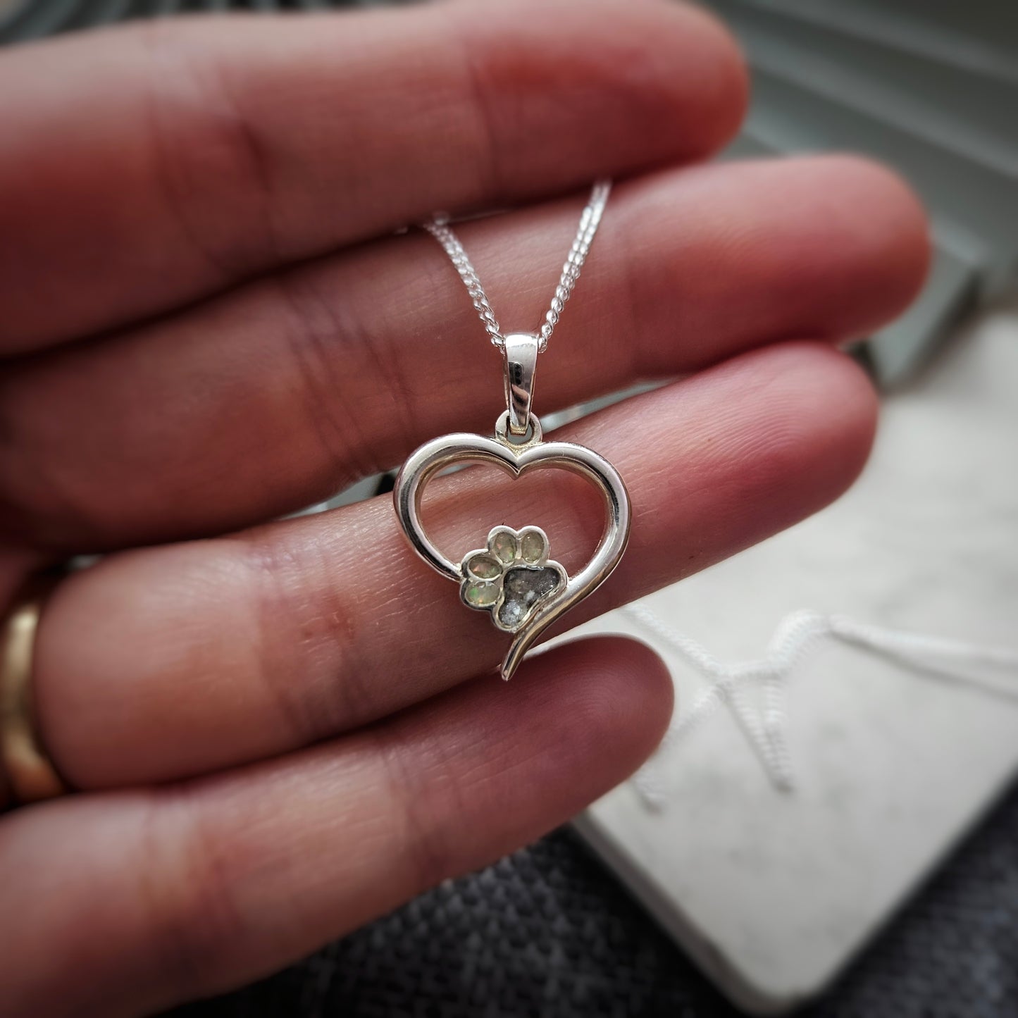 Silver heart-shaped pendant with a paw print design held in a hand.