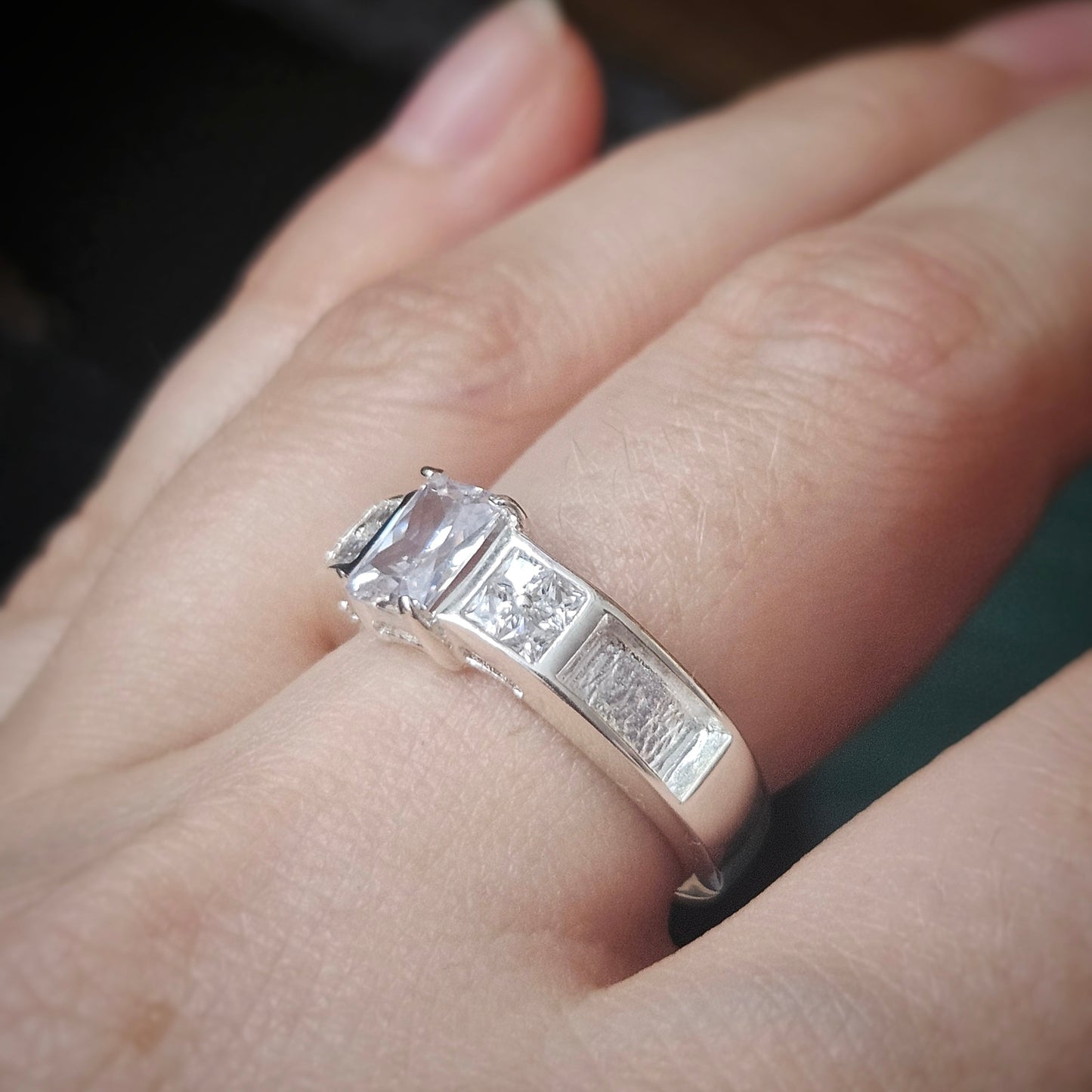 Silver ring with a large diamond on a finger against a blurred background