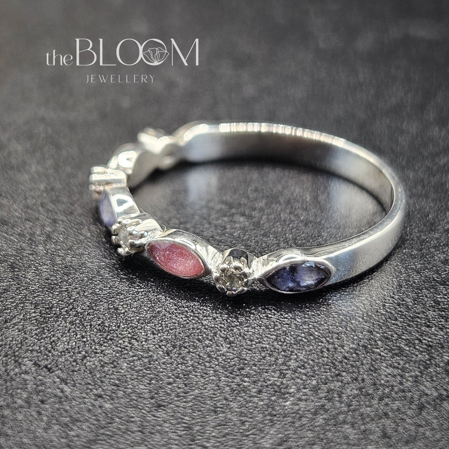Silver ring with embedded stones on a dark textured surface, branded 'the BLOOM JEWELLERY'.