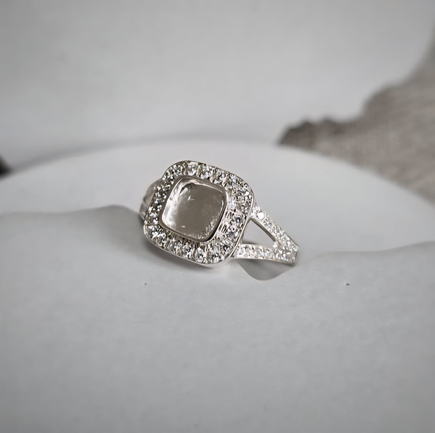 Silver ring with a square-shaped center and diamond accents on a light gray background