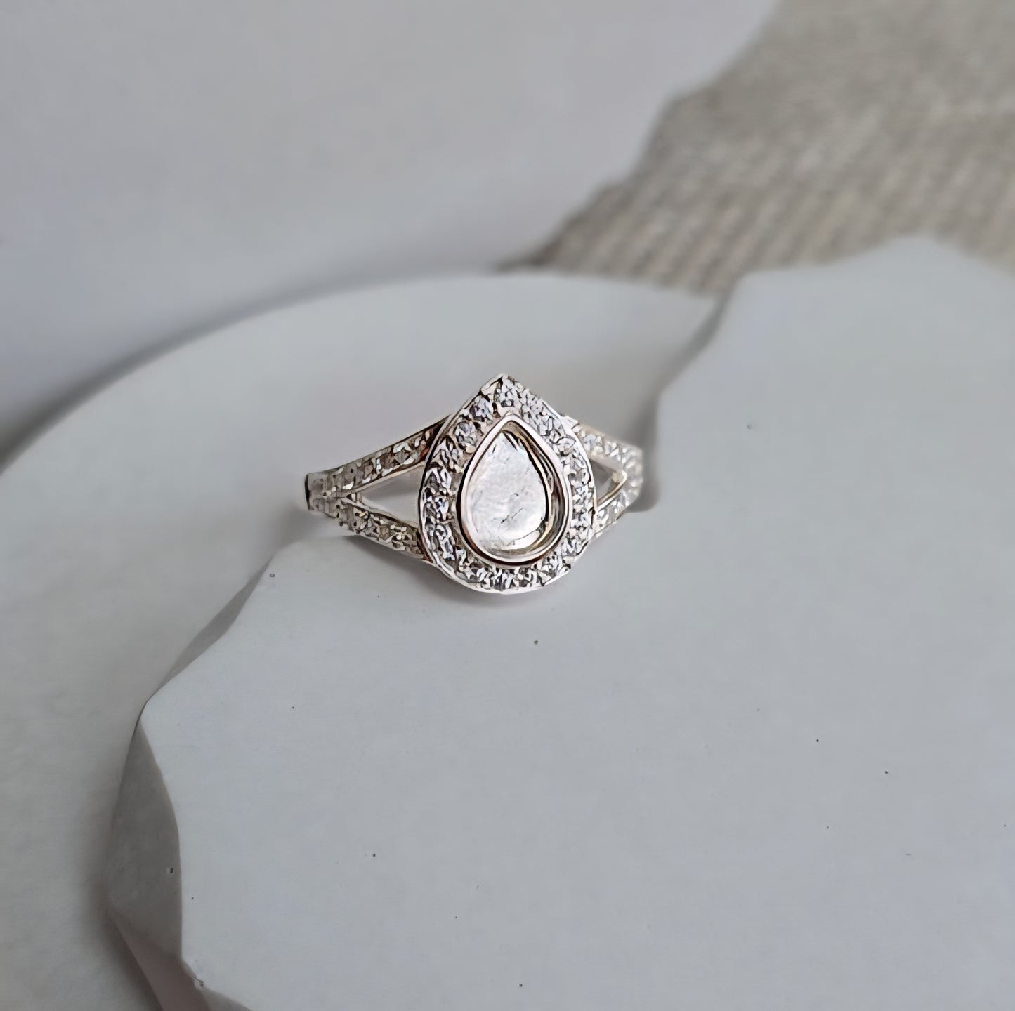 Silver ring with a teardrop-shaped center stone on a white surface