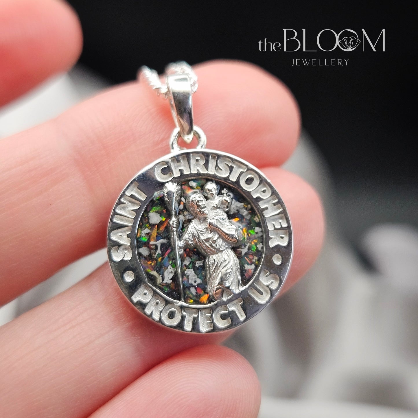Silver Saint Christopher pendant held in a hand with 'the Bloom Jewellery' branding.