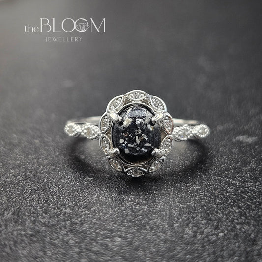 Silver ring with central gemstone on a dark textured background, branded 'the BLOOM JEWELLERY'.