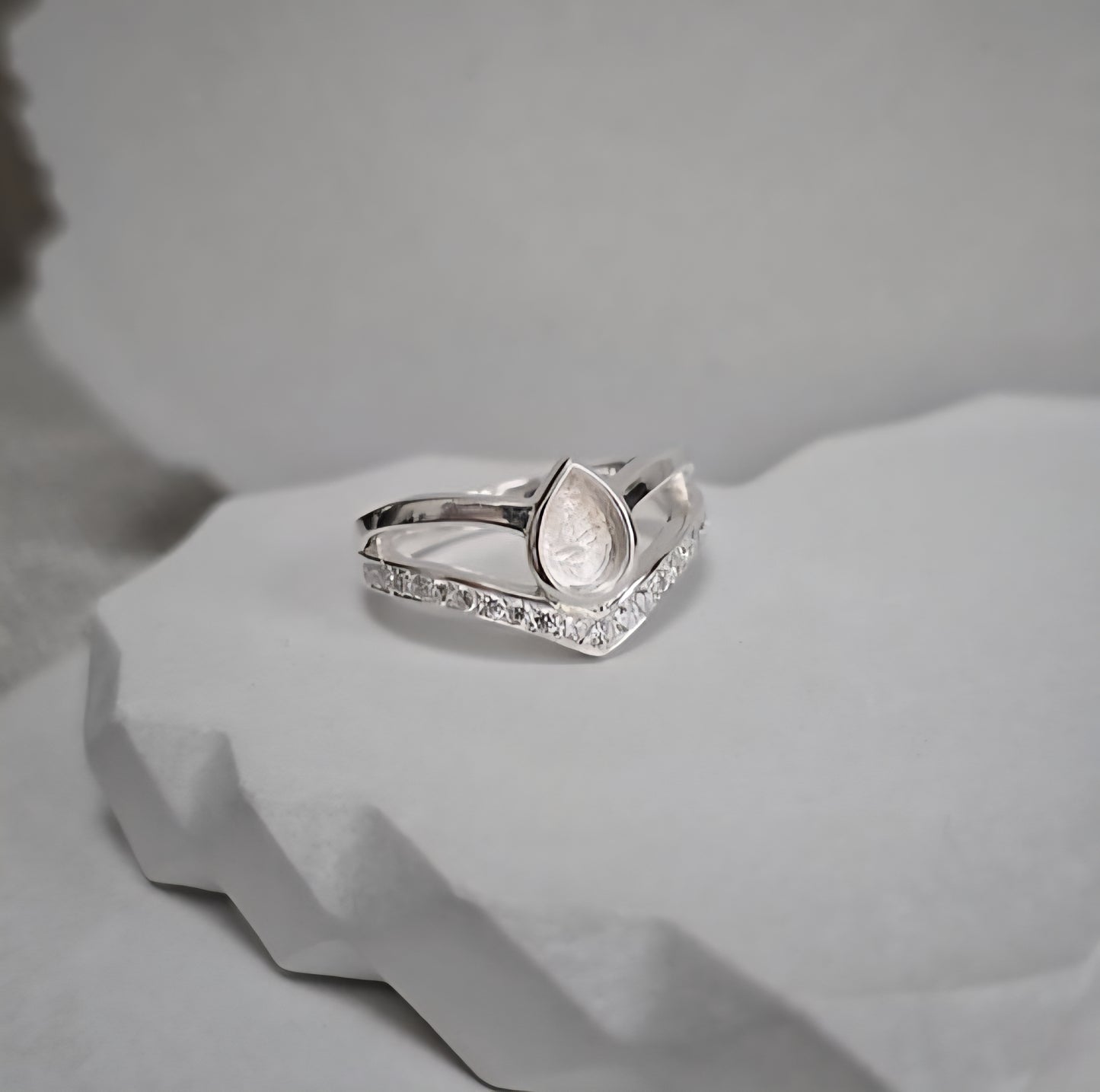 Silver ring with a teardrop design and small diamonds on a light gray background