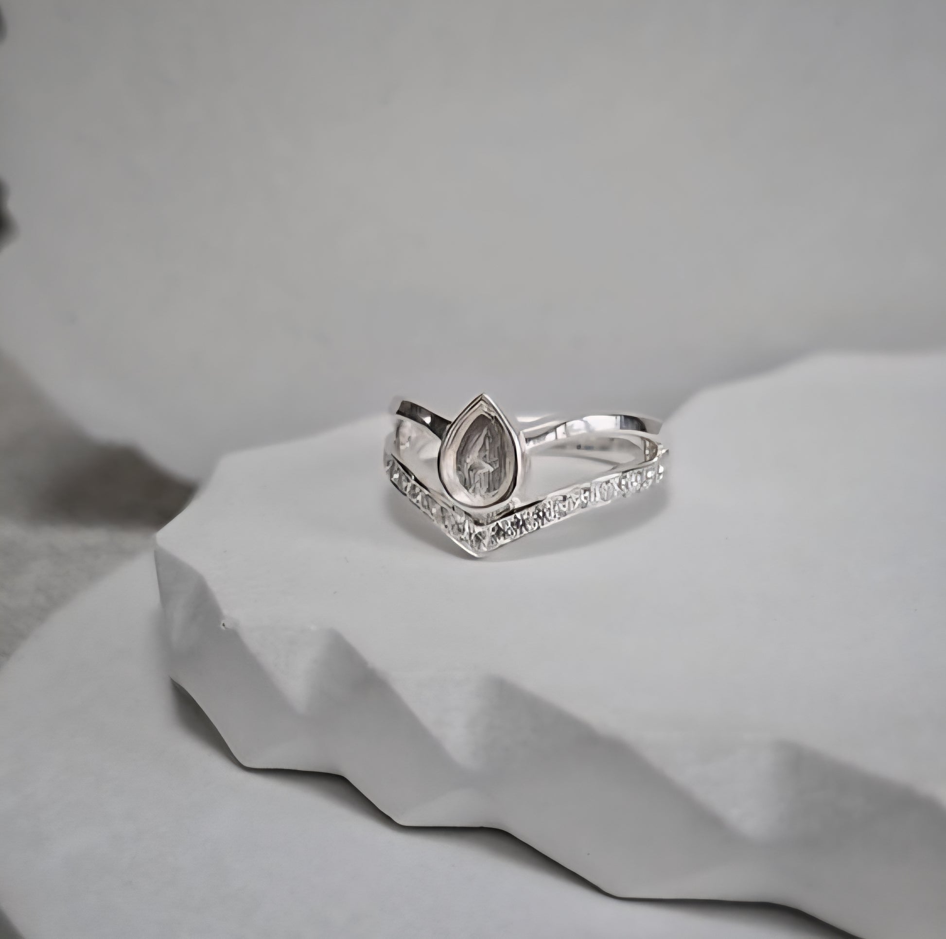 Silver ring with a teardrop-shaped center stone on a textured gray surface