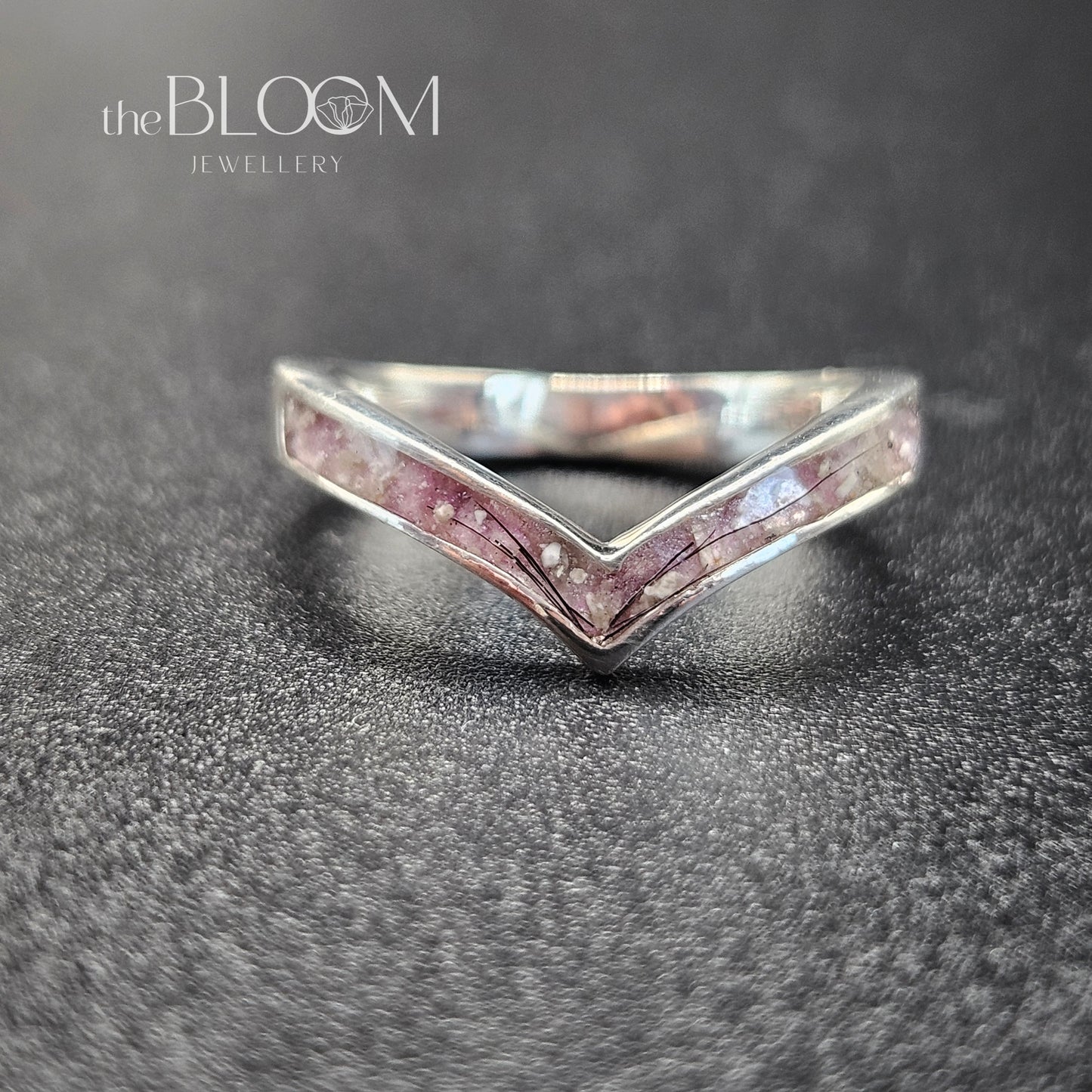 Silver ring with pink gemstones on a dark textured surface, branded 'the BLOOM Jewellery'.