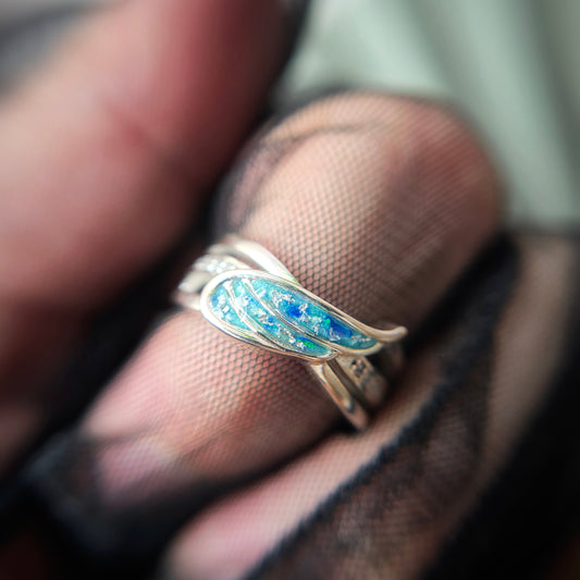 Close-up of a silver ring with blue and green enamel on a finger.