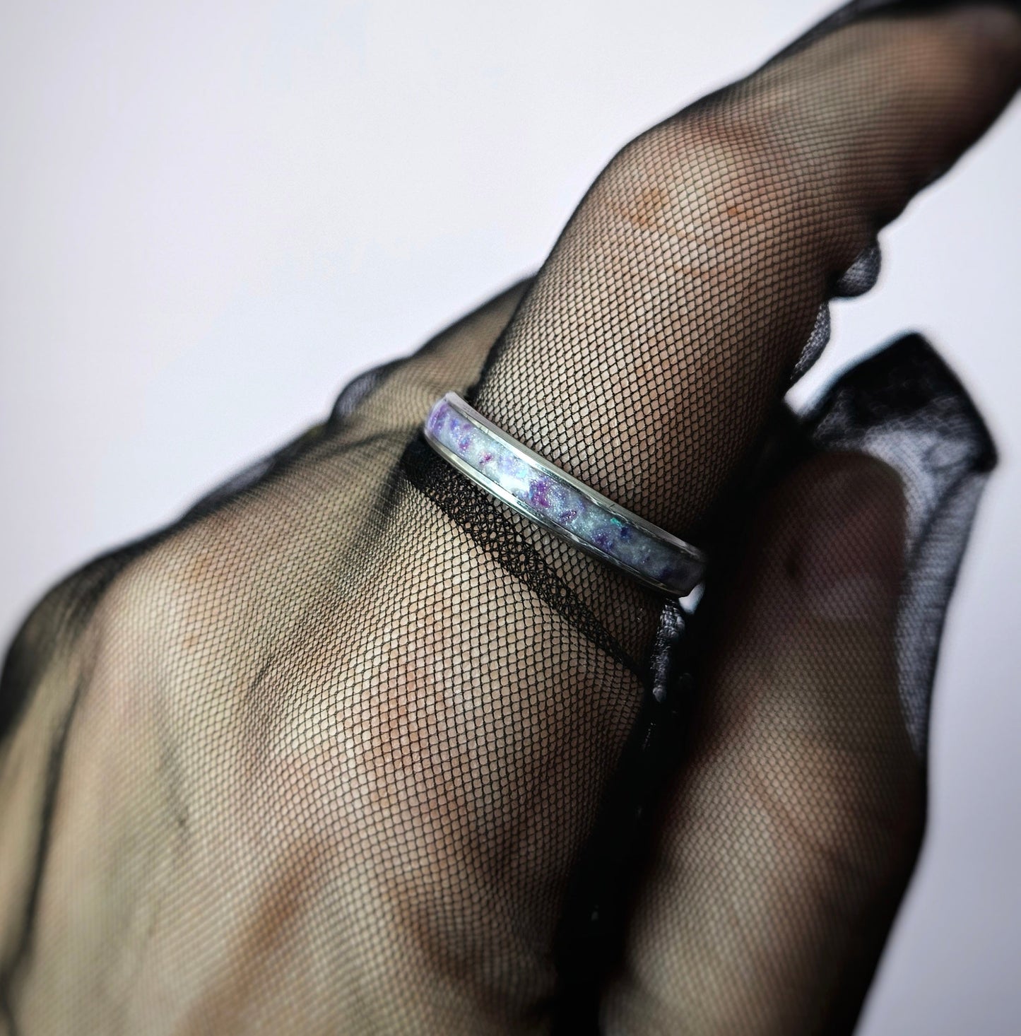 Close-up of a hand wearing a black mesh glove with a silver ring on a white background