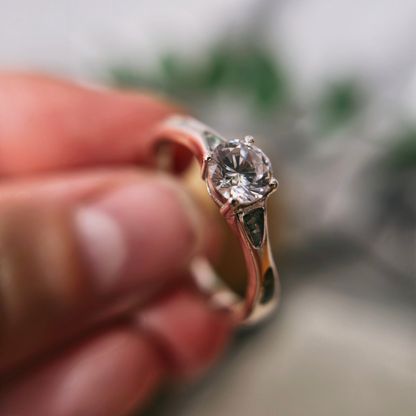 Close-up of a diamond ring held between fingers with a blurred background