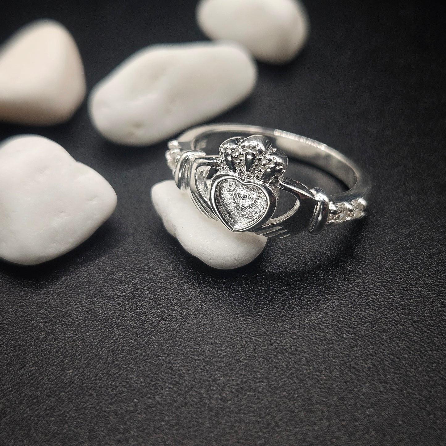 Silver ring with a heart-shaped gemstone on pebbles
