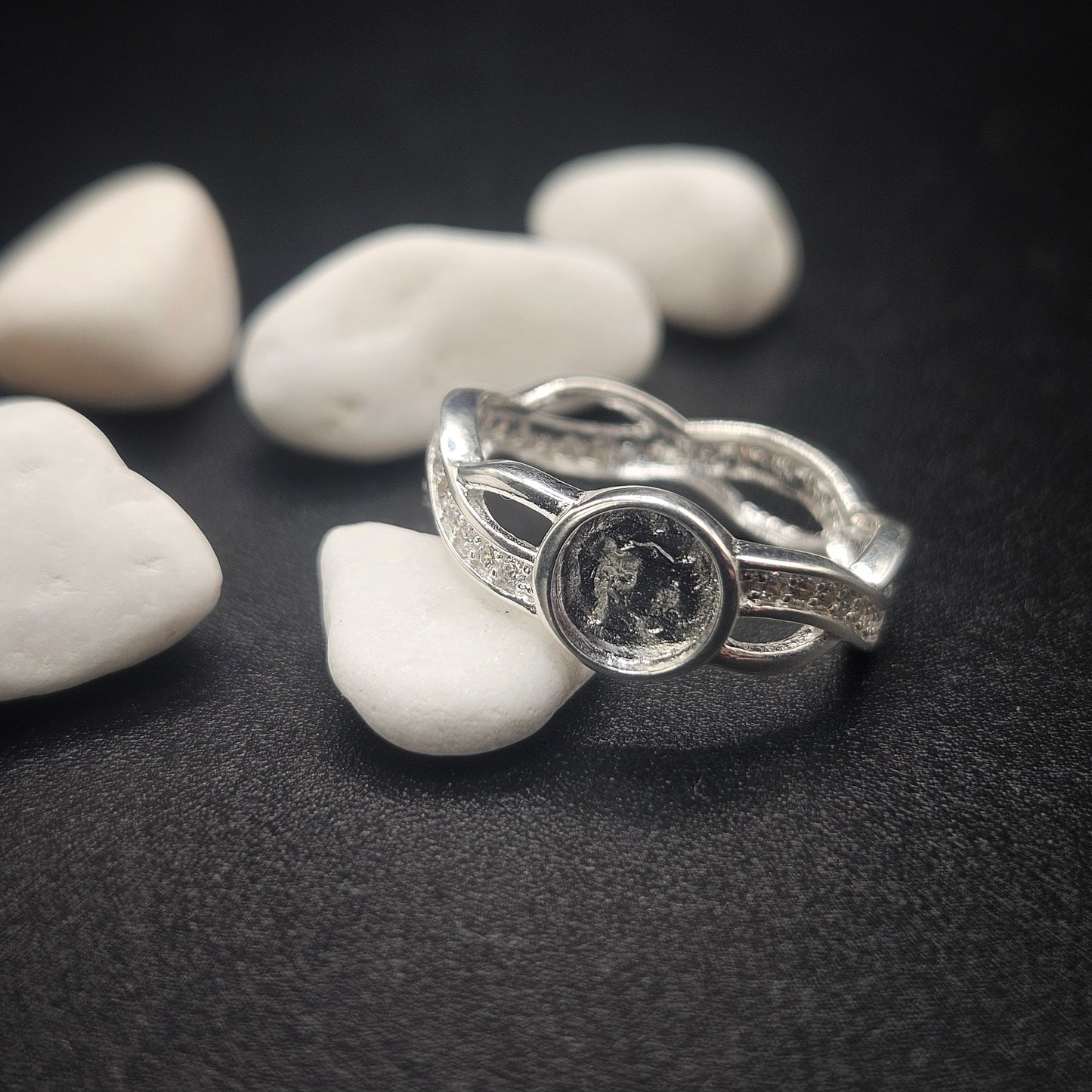 Silver ring with a circular design on pebbles and a dark surface