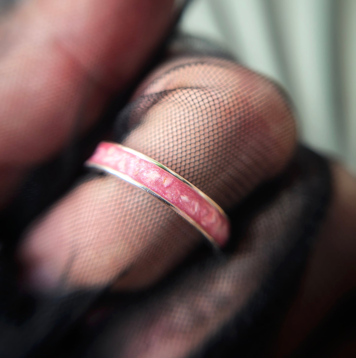 Close-up of a hand wearing a pink ring with a blurred background