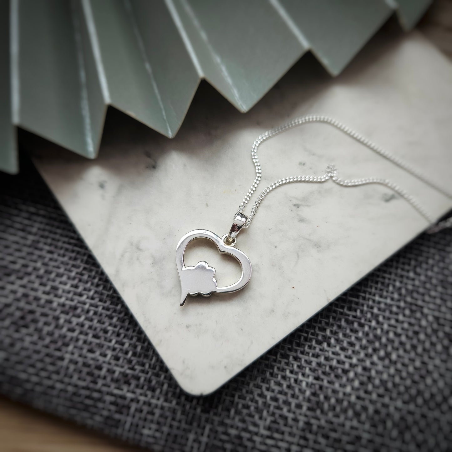 Silver heart-shaped necklace with a paw print design on a textured surface.