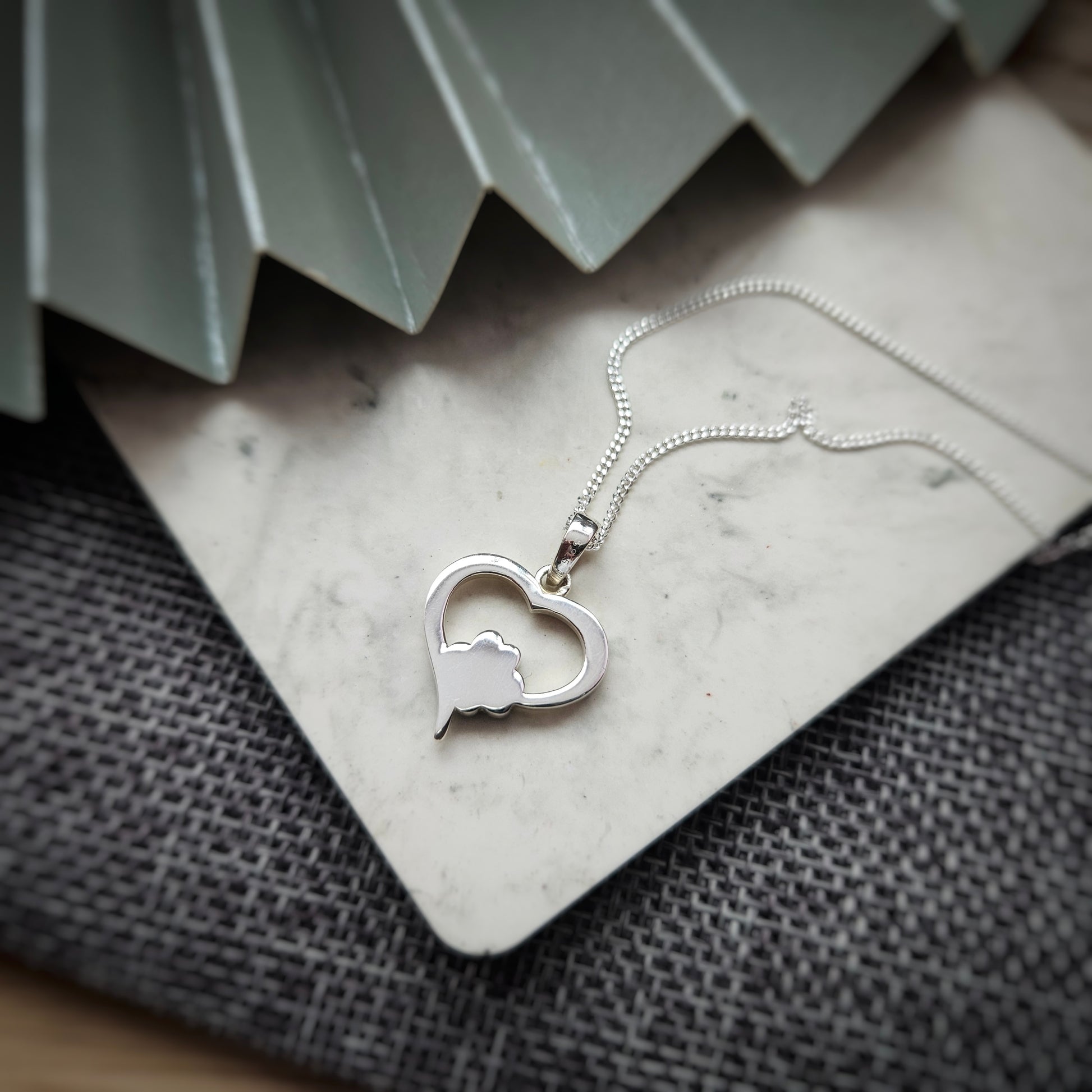 Silver heart-shaped necklace with a paw print design on a textured surface.