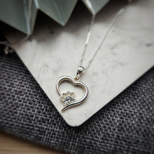 Silver heart-shaped necklace with a paw print design on a textured surface