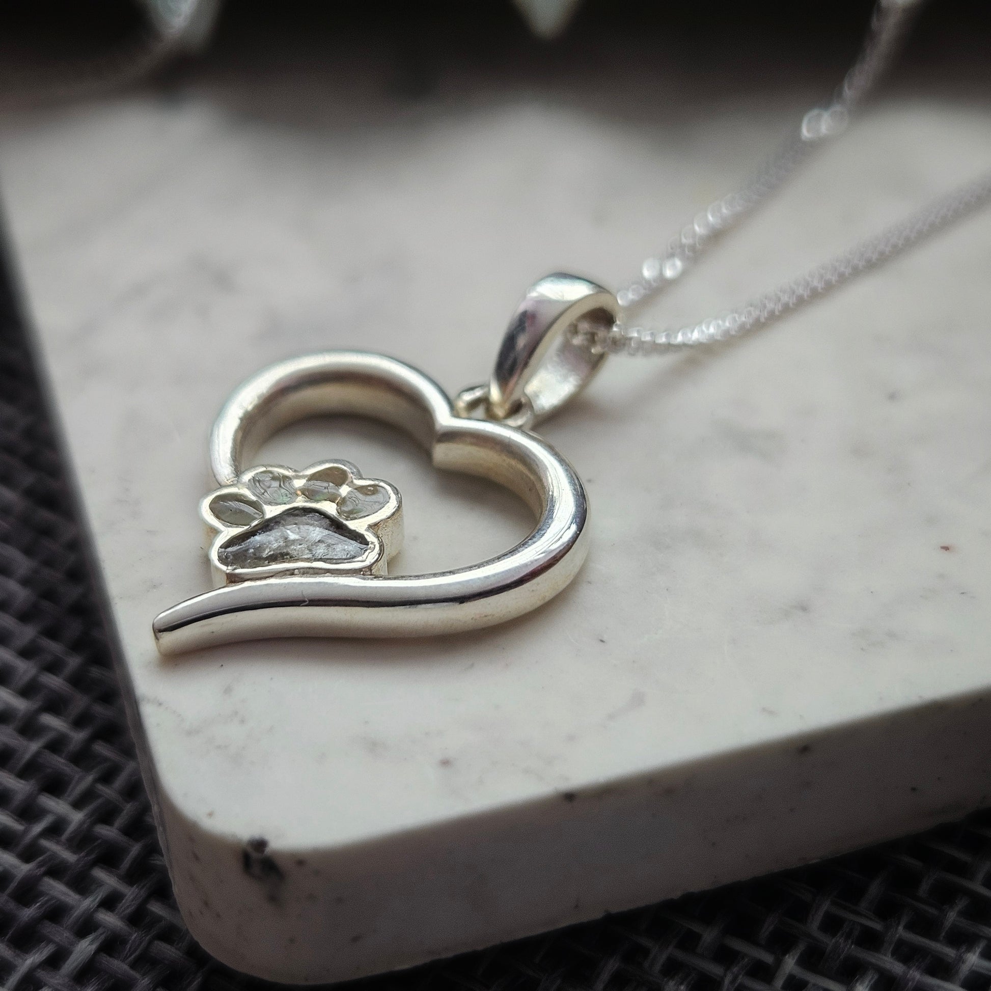 Silver necklace with a heart and paw print pendant on a textured surface
