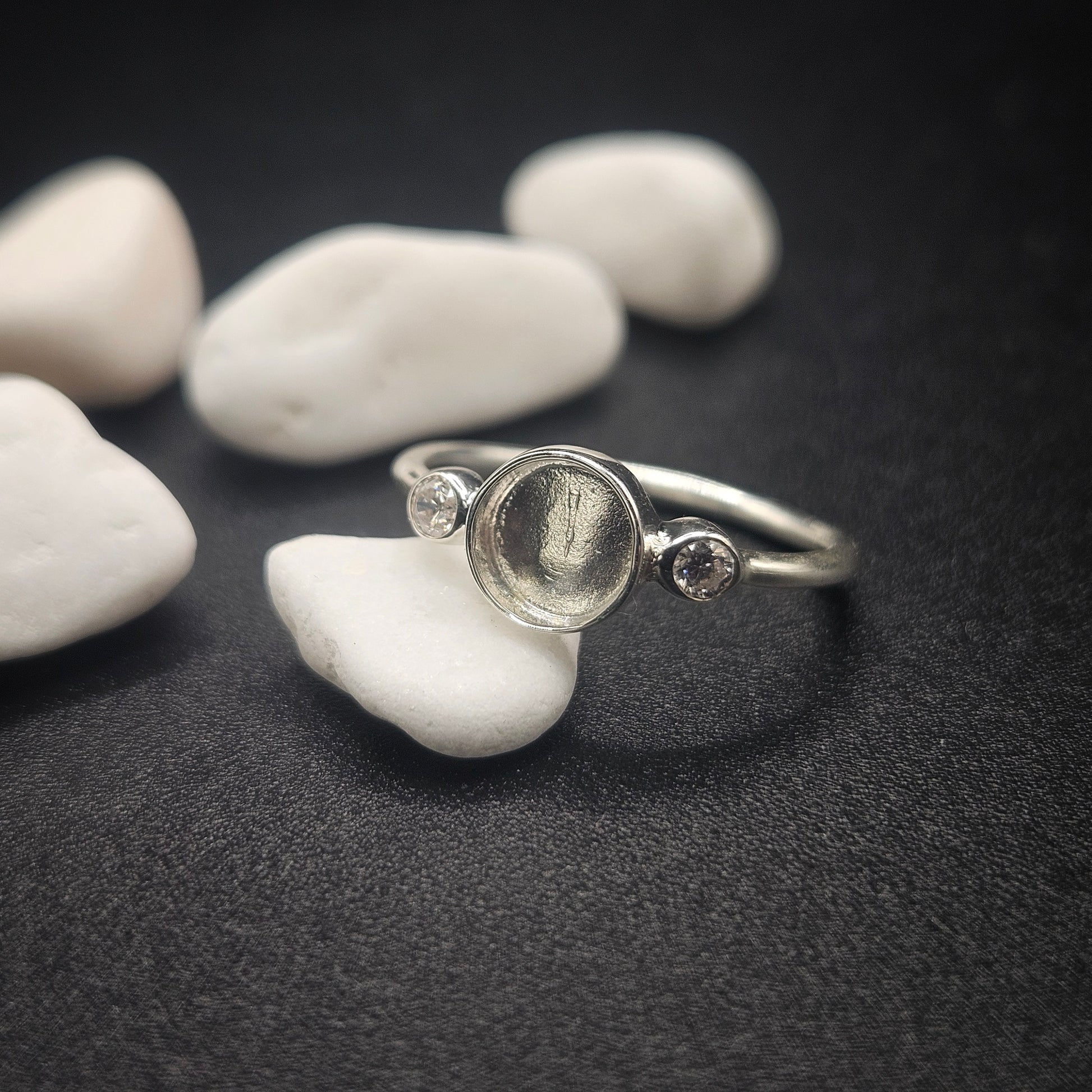 Silver ring with circular design on a dark surface with white stones
