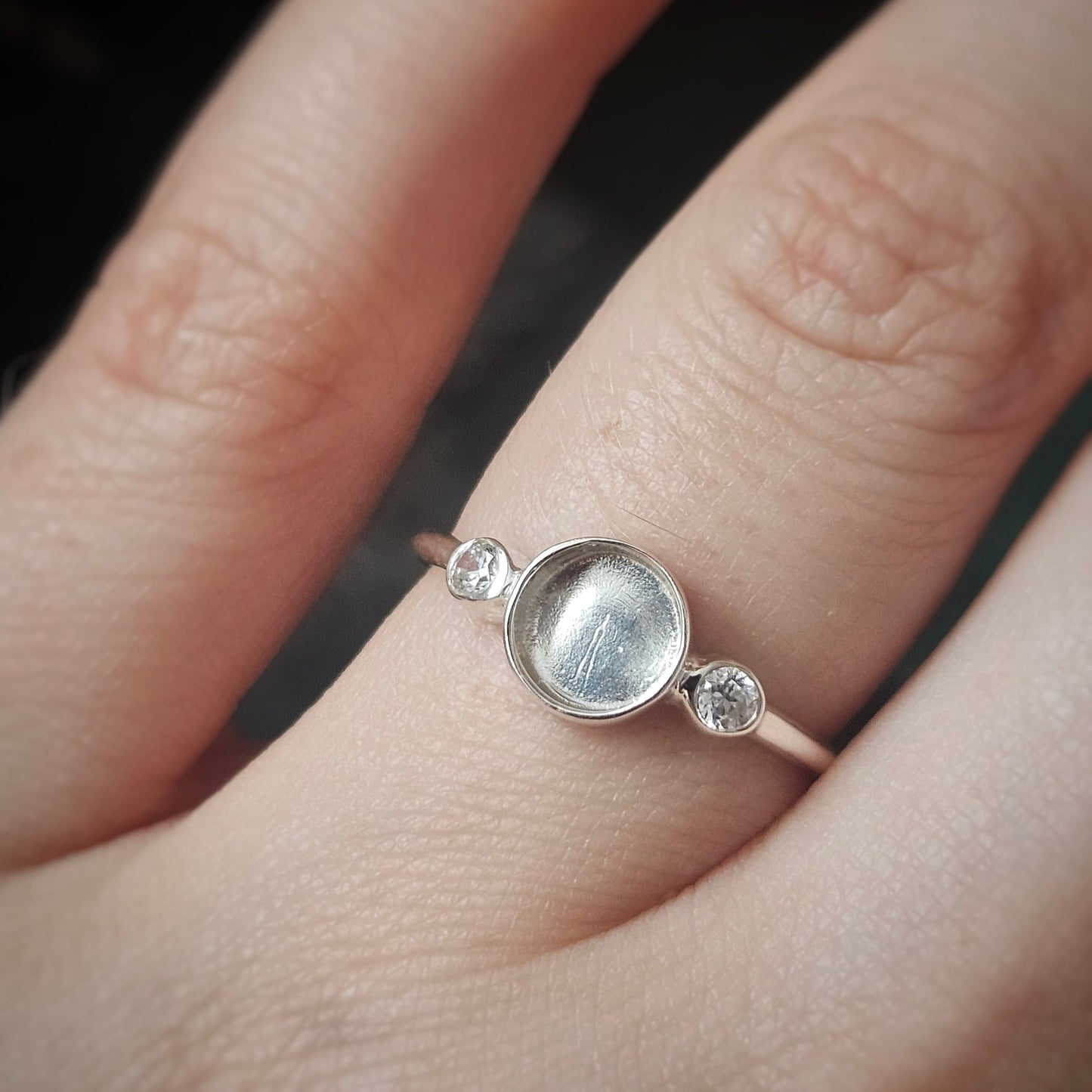 Silver ring with a central gemstone and smaller stones on a finger