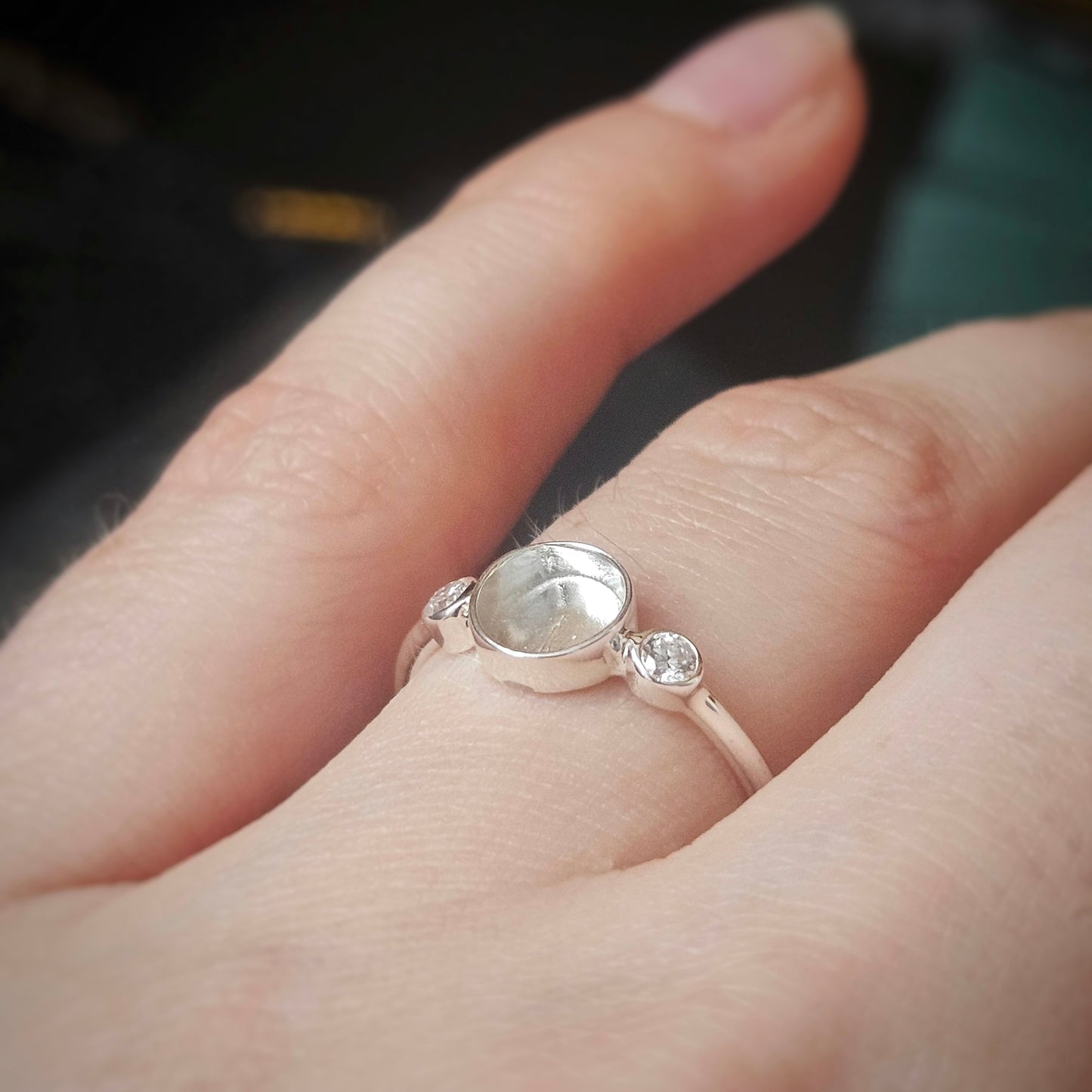 Silver ring with a gemstone on a person's finger against a blurred background