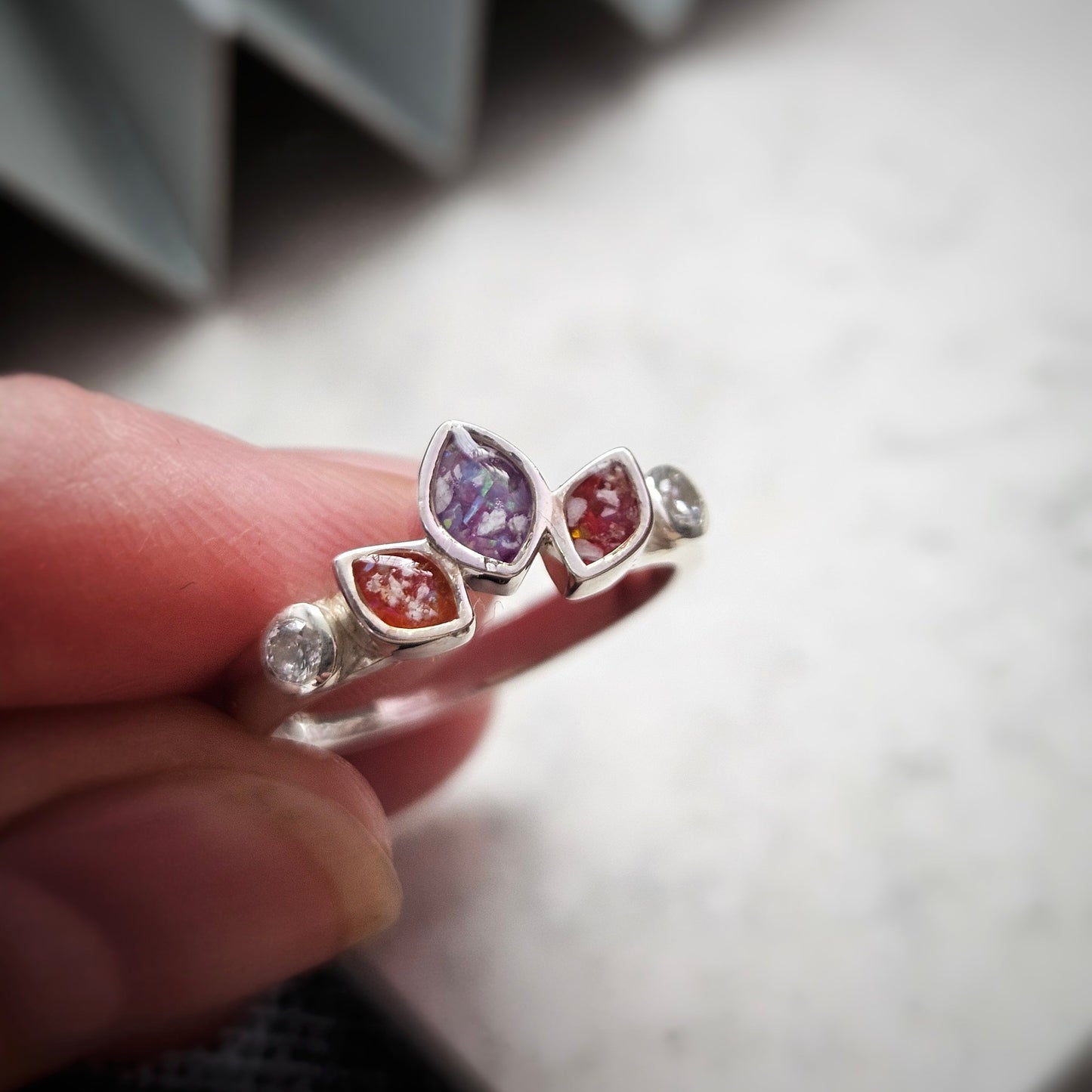 Silver ring with colorful gemstones held by a hand against a neutral background