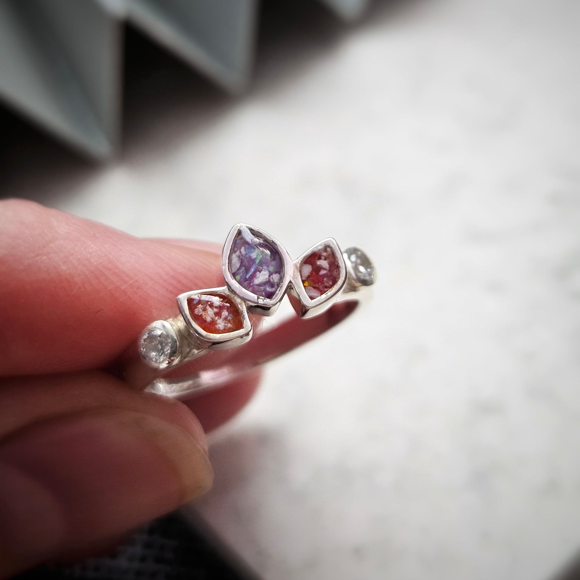 Silver ring with colorful gemstones held by a hand against a neutral background