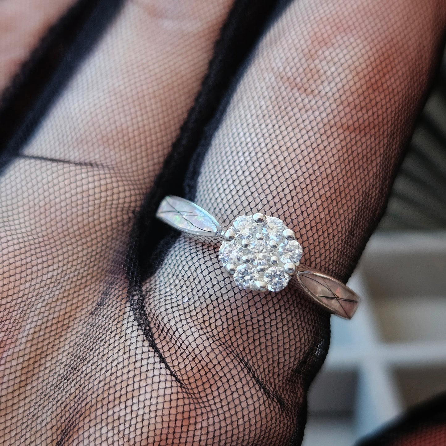Silver ring with a diamond on a hand wearing black mesh gloves.