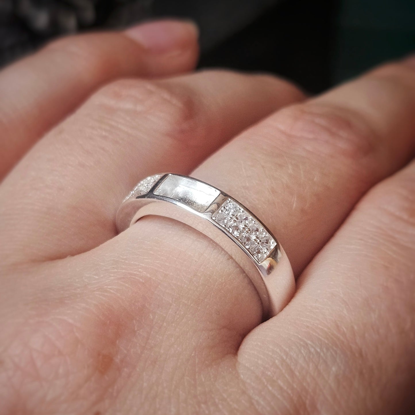 Silver ring with diamond accents on a finger against a blurred background