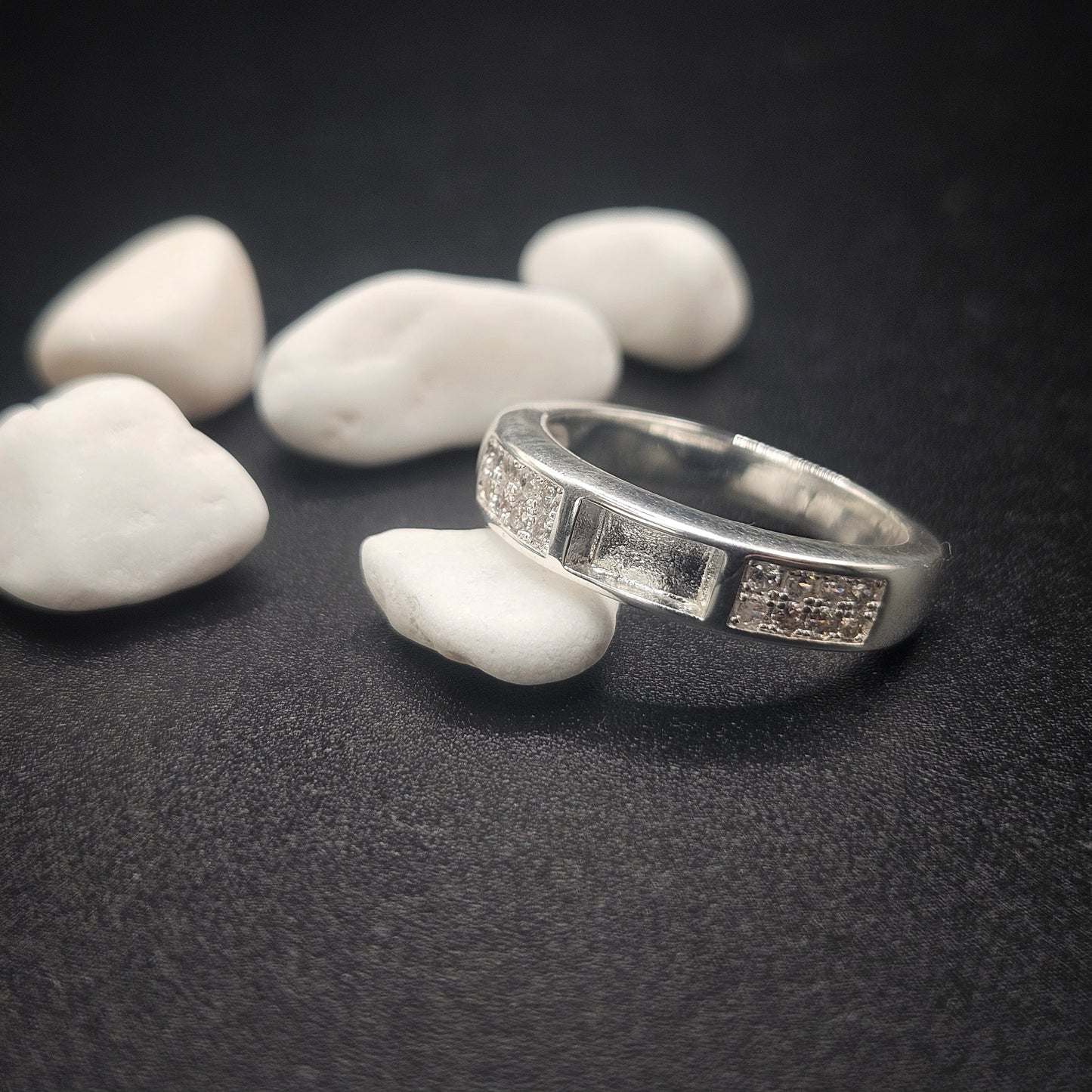 Silver ring with engraved design on a dark surface with white stones