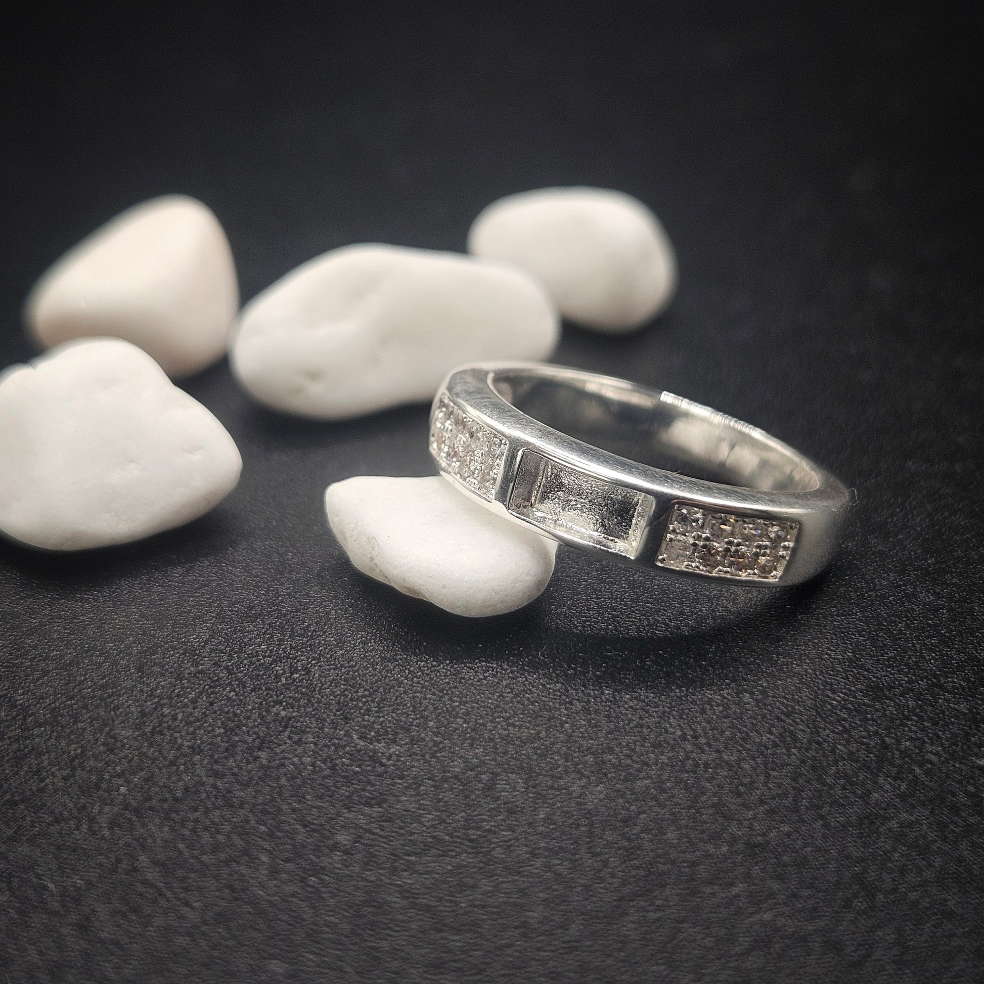 Silver ring with engraved design on a dark surface with white stones