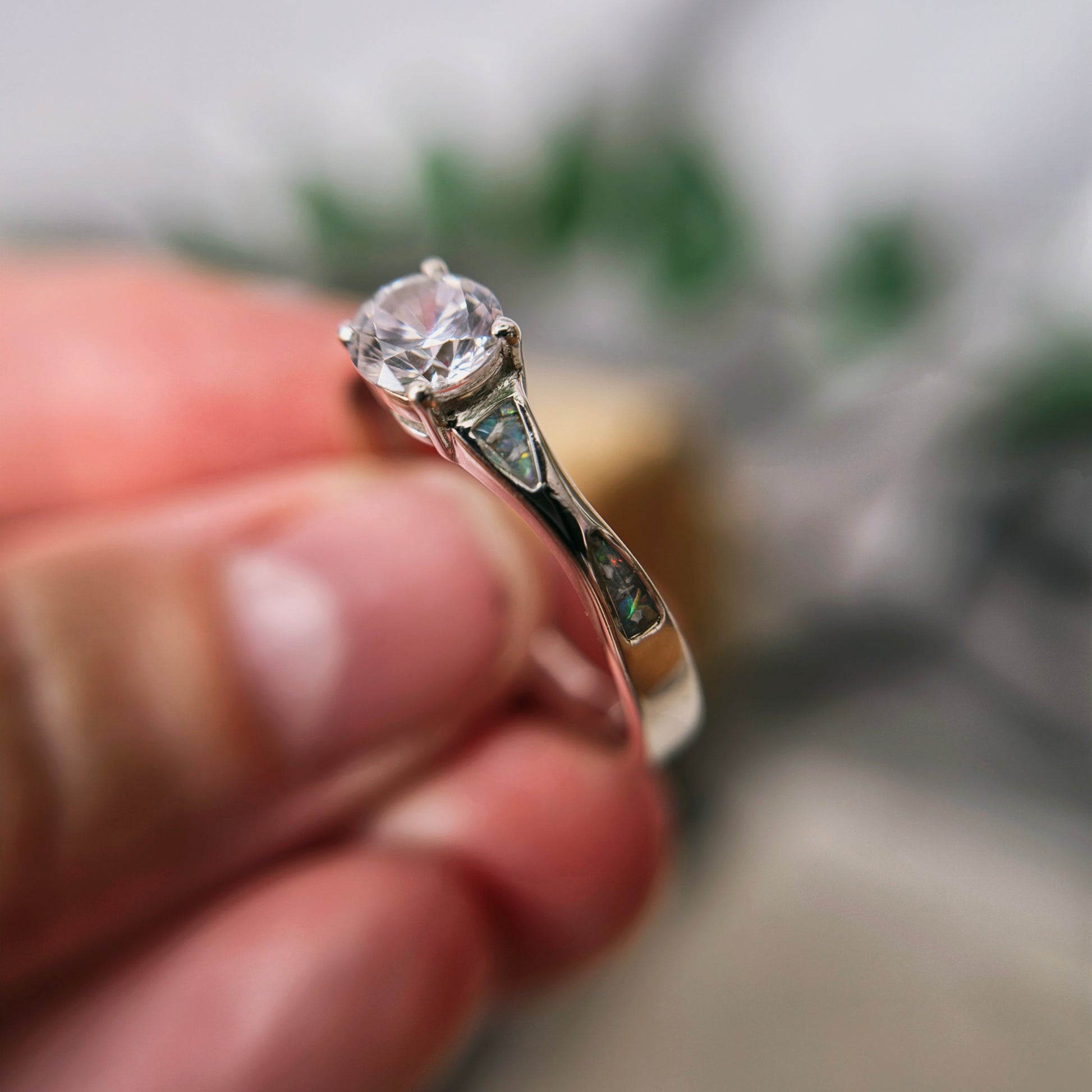 Silver ring with a diamond held between fingers against a blurred background