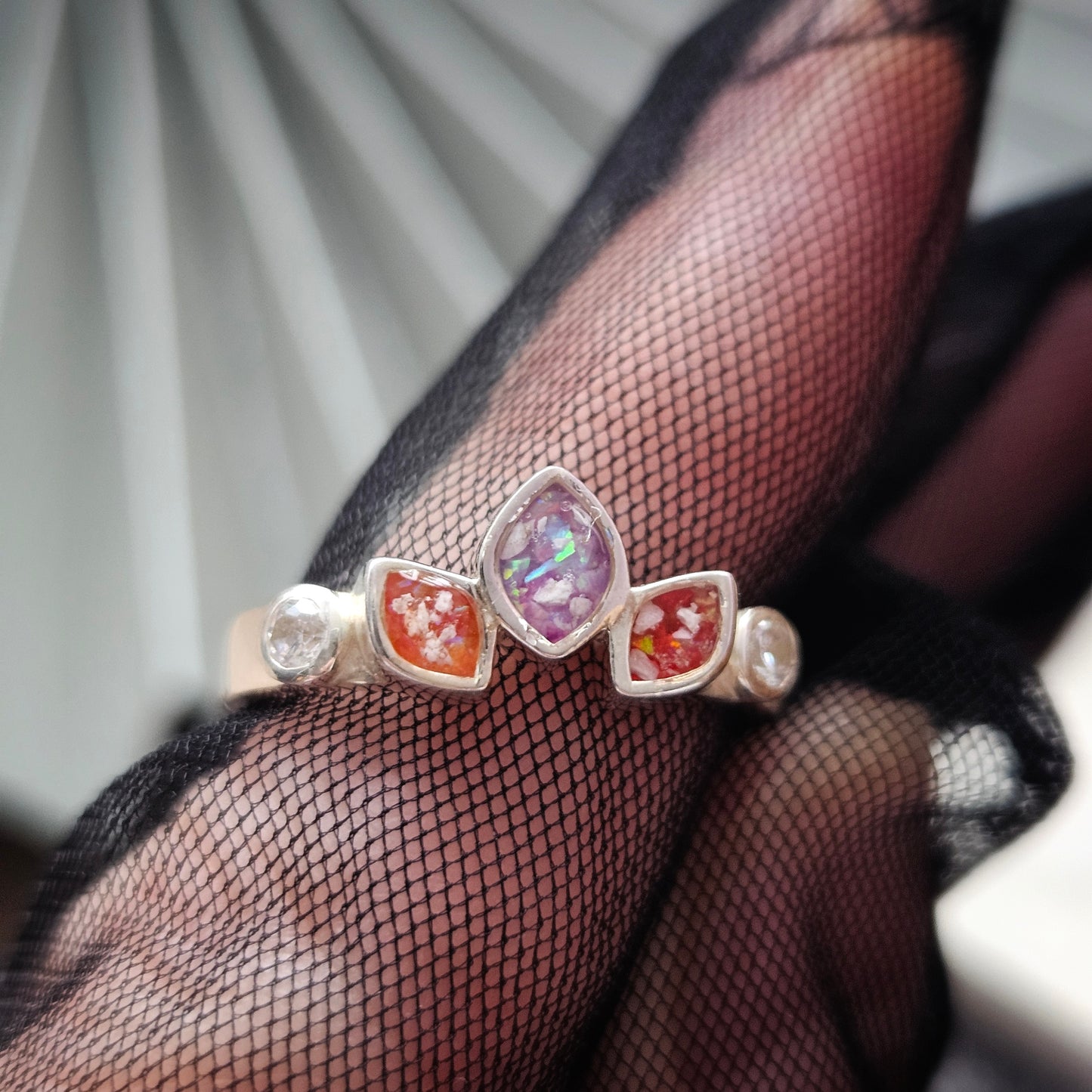 Three gemstone rings held by a hand wearing black fishnet gloves.