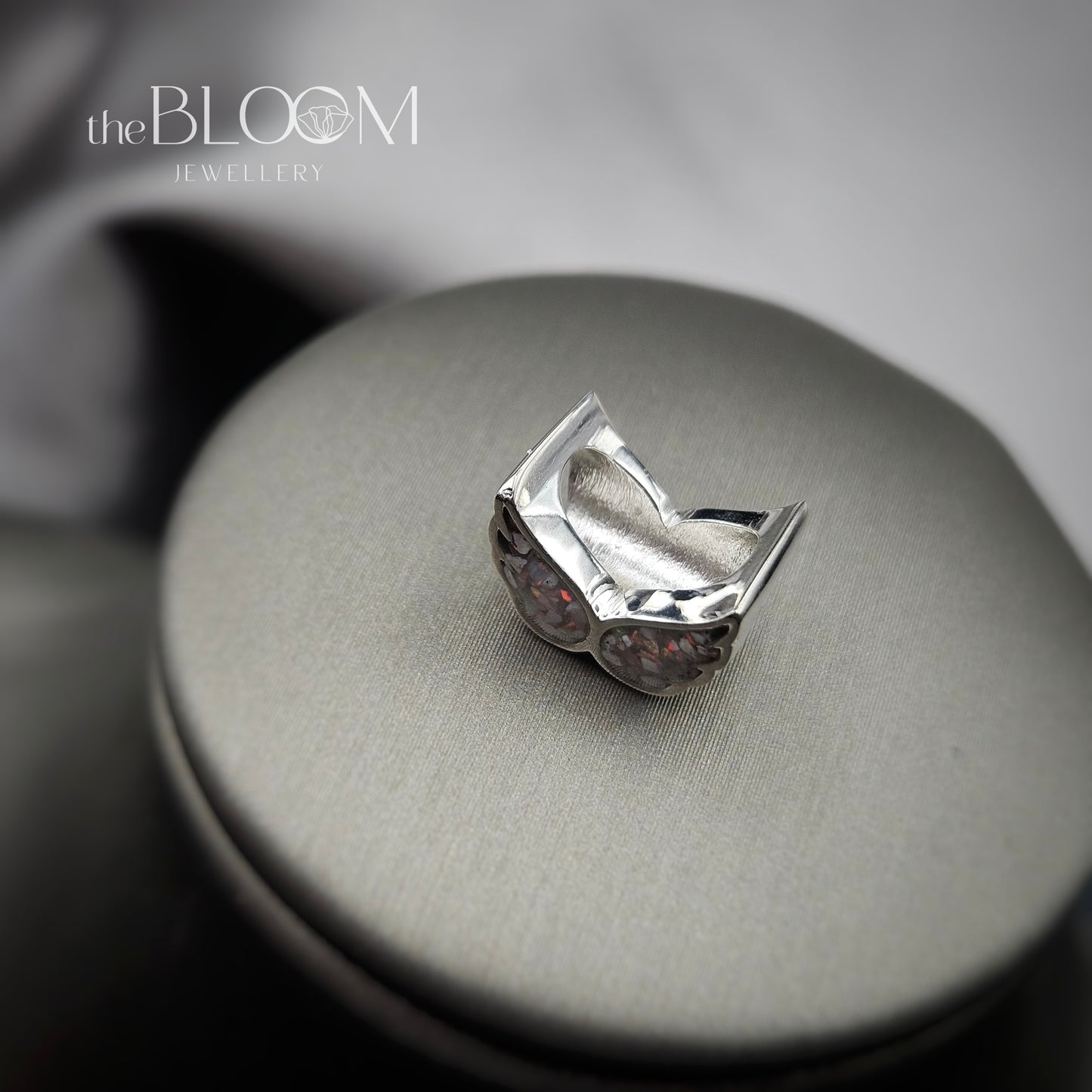 Silver ring with embedded stones on a metallic surface, branded 'the BLOOM JEWELLERY'.