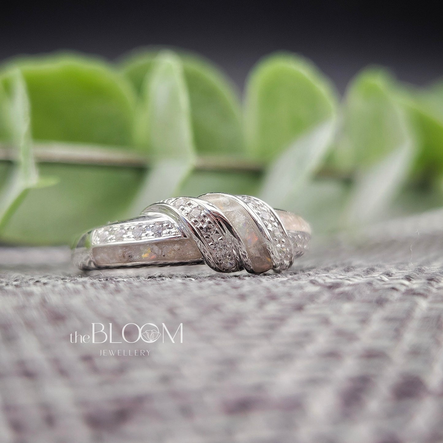 Silver ring with diamonds on a textured surface with green leaves in the background