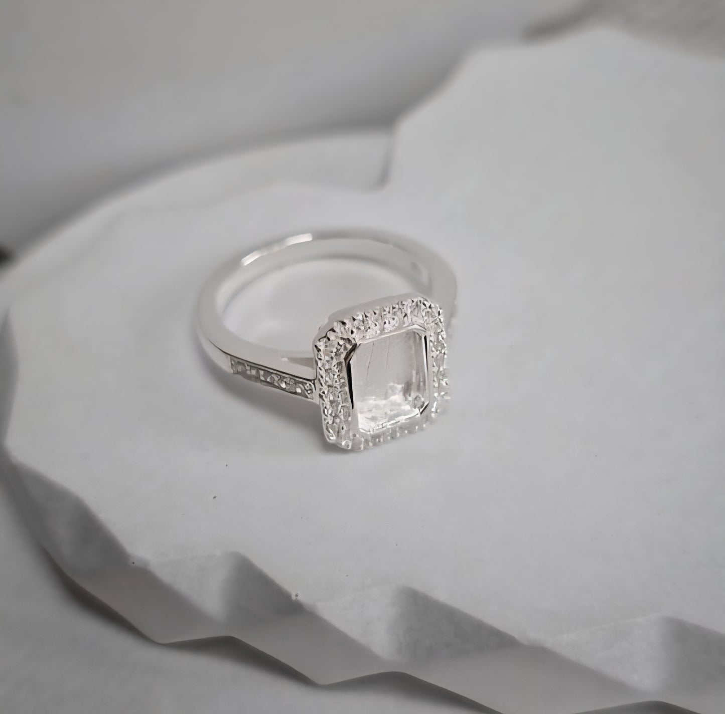Silver ring with a square-cut gemstone on a textured white surface
