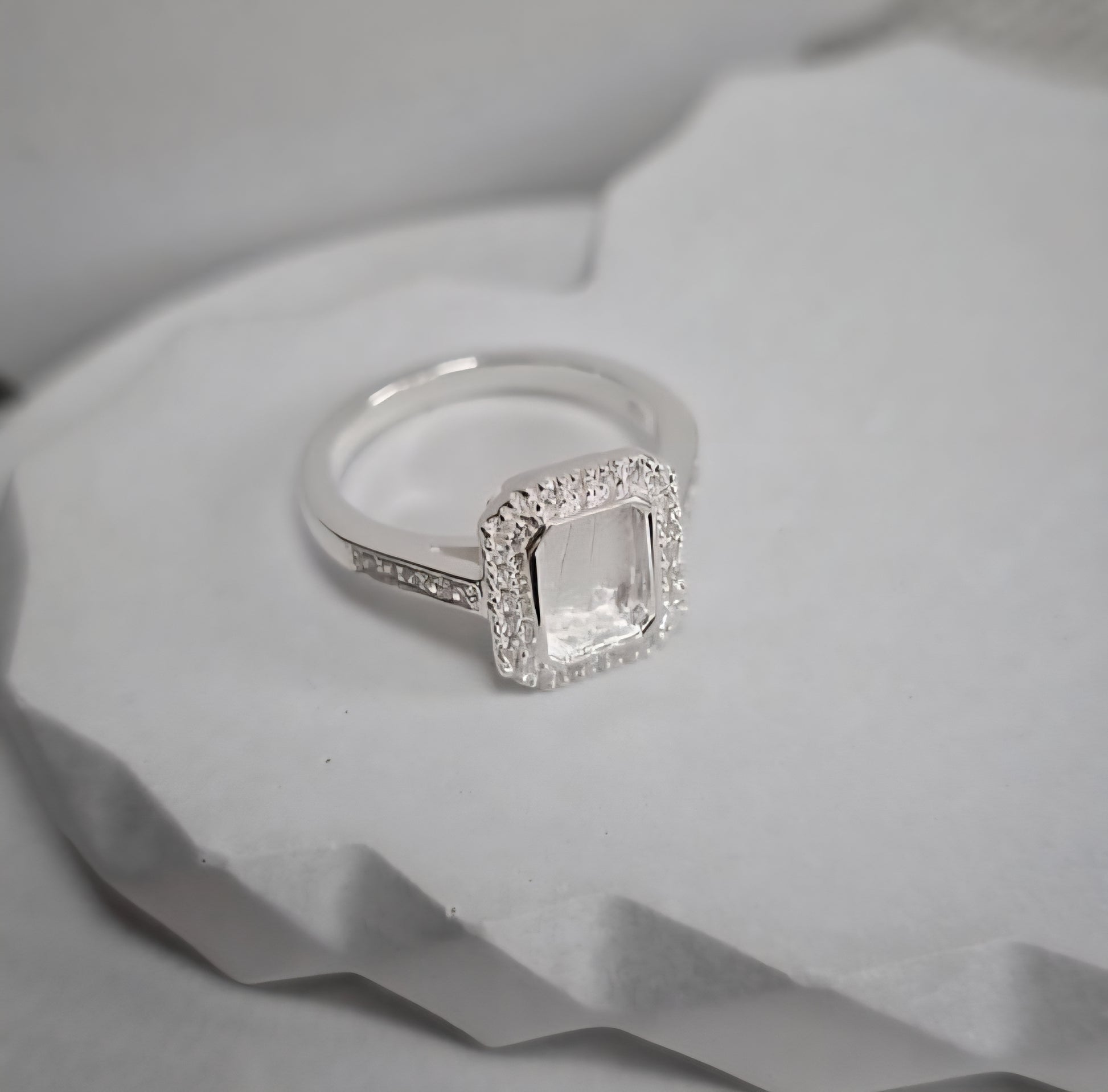 Silver ring with a square-cut gemstone on a textured white surface