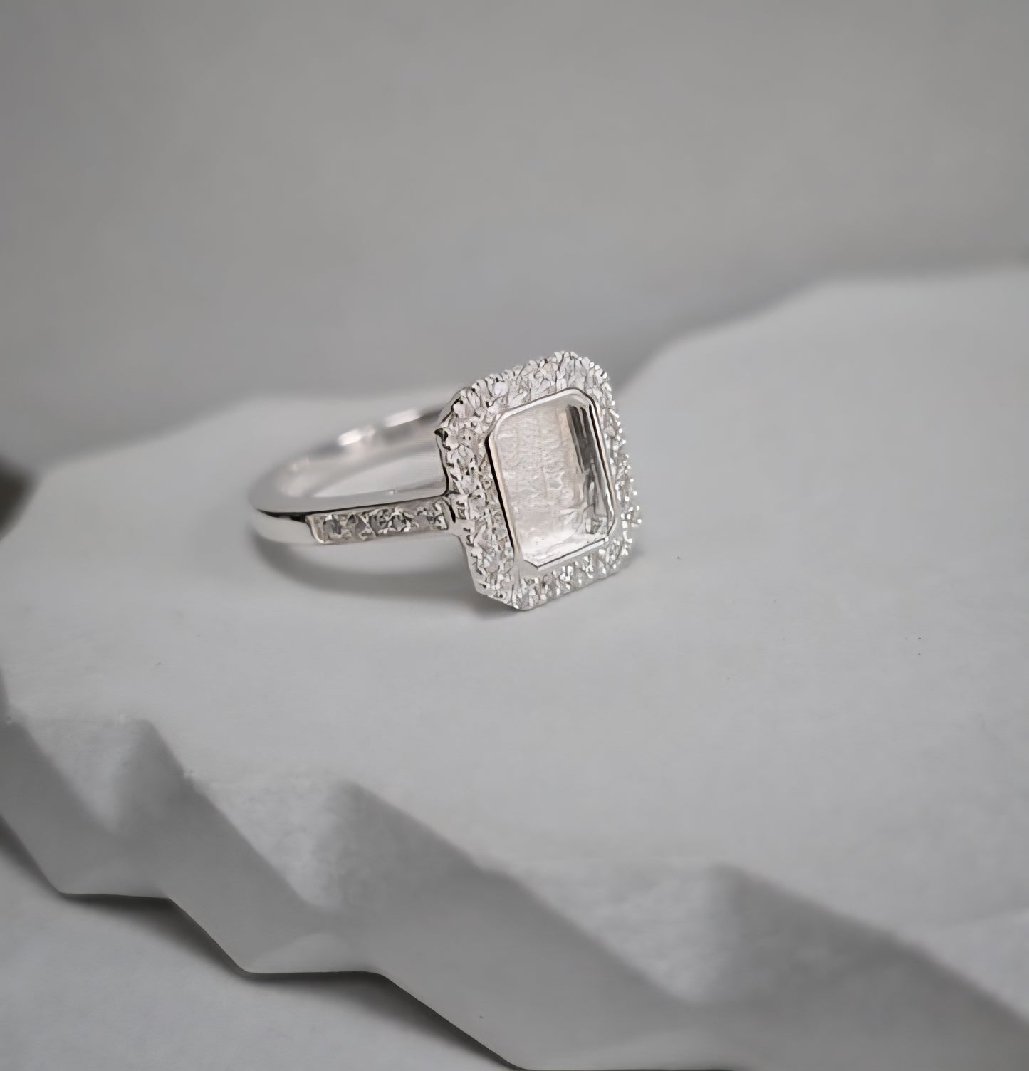 Silver ring with a rectangular gemstone on a textured gray surface