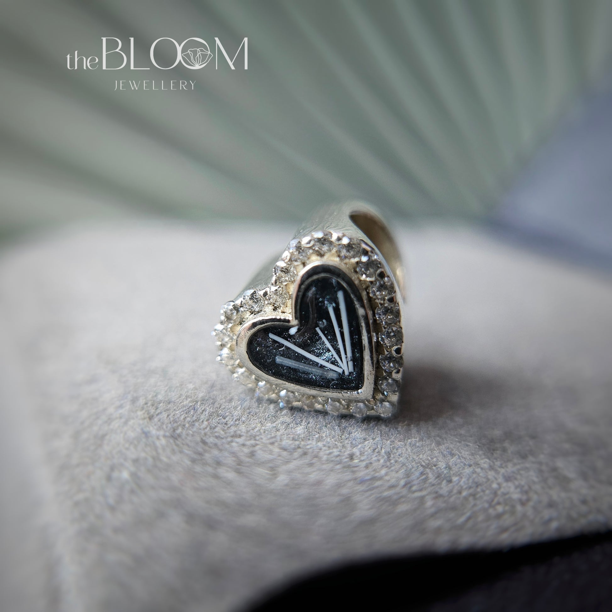 Heart-shaped silver and black keepsake charm on a textured surface with 'the BLOOM JEWELLERY' logo.