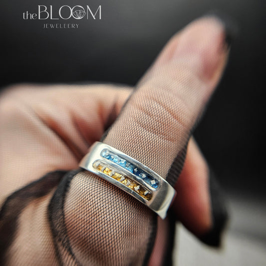 Silver ring with gemstones on a finger, branded 'the BLOOM JEWELLERY'.