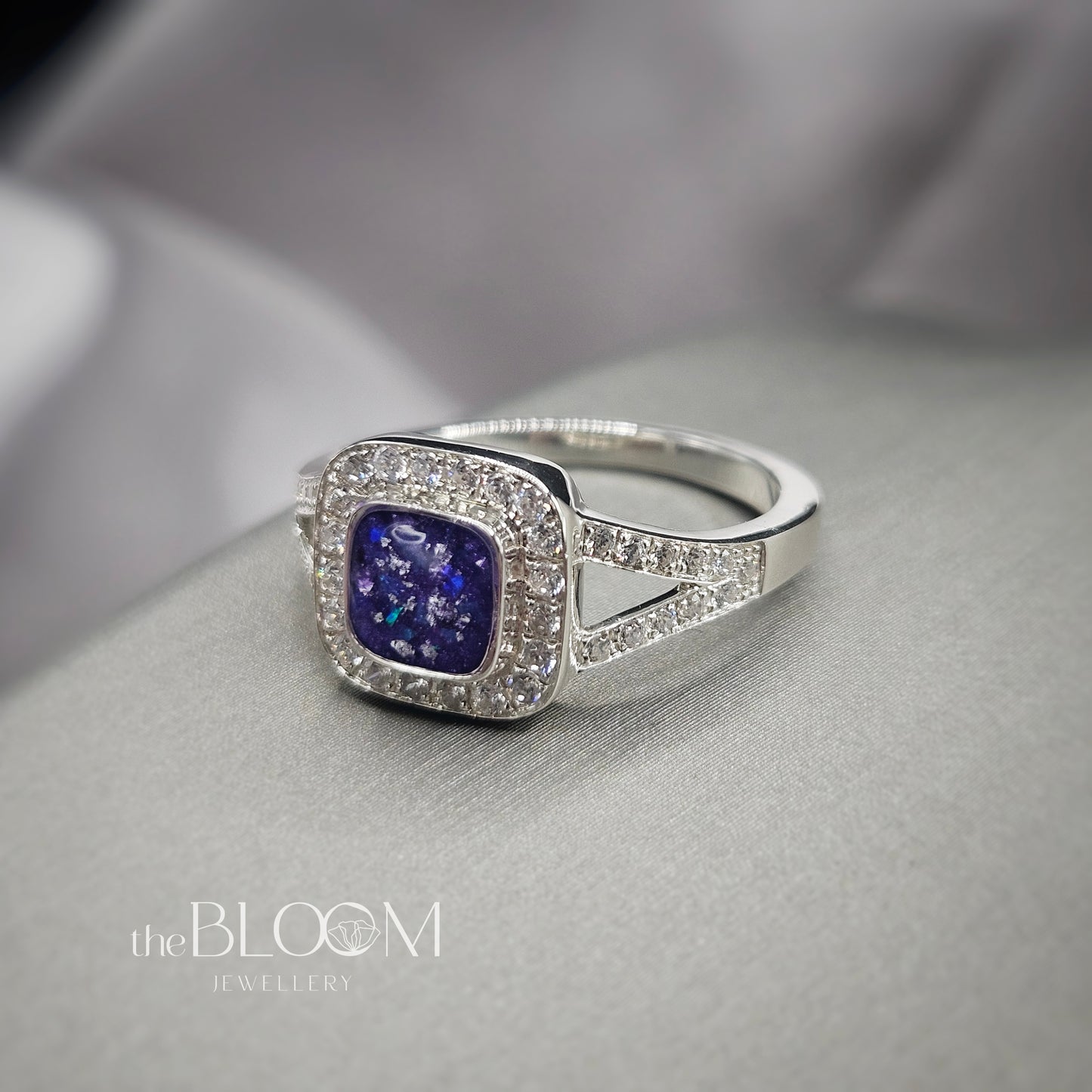 Silver ring with a purple gemstone on a gray surface, branded 'the BLOOM Jewellery'.