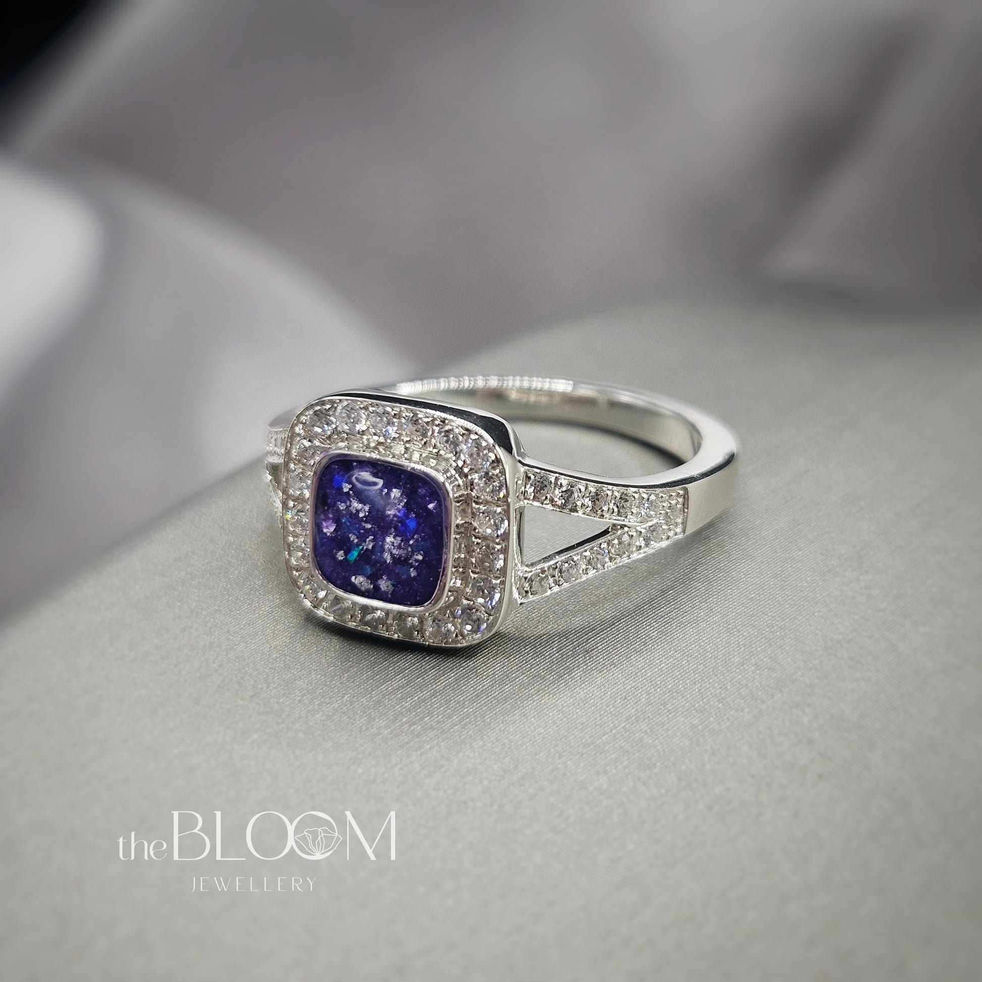 Silver ring with a purple gemstone on a gray surface, branded 'the BLOOM Jewellery'.