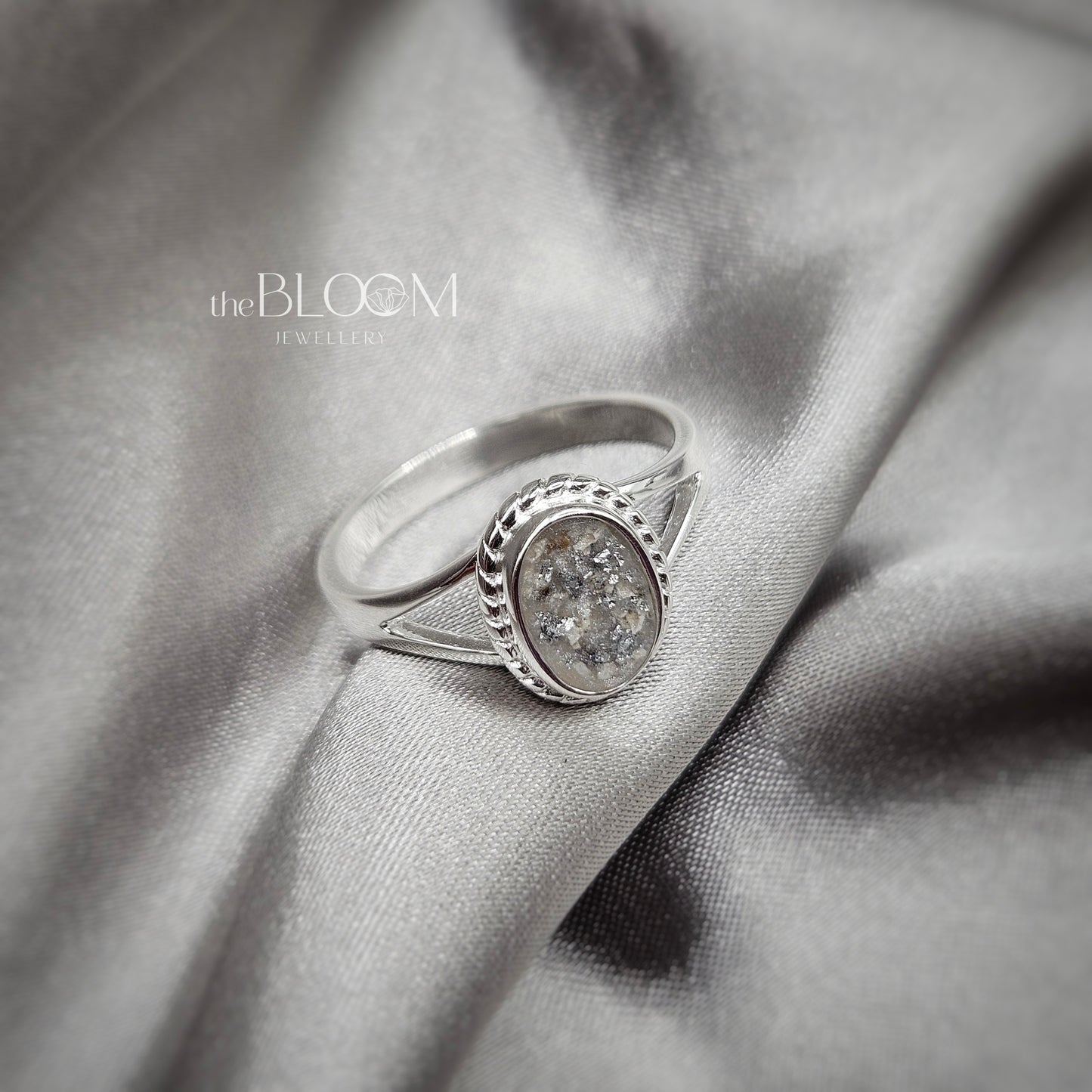 Silver ring with a diamond on a gray fabric background, branded 'the BLOOM Jewellery'.