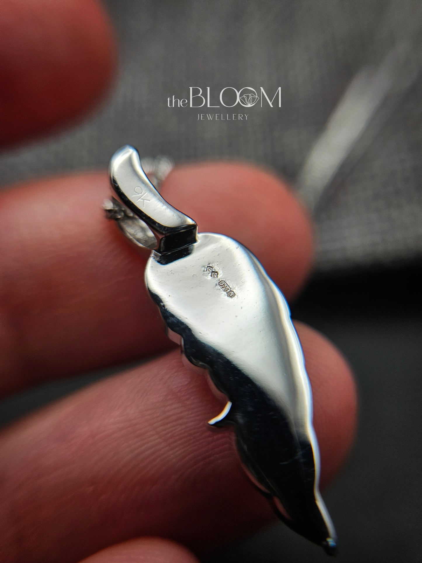 white gold pendant held between fingers with 'The Bloom Jewellery' branding.