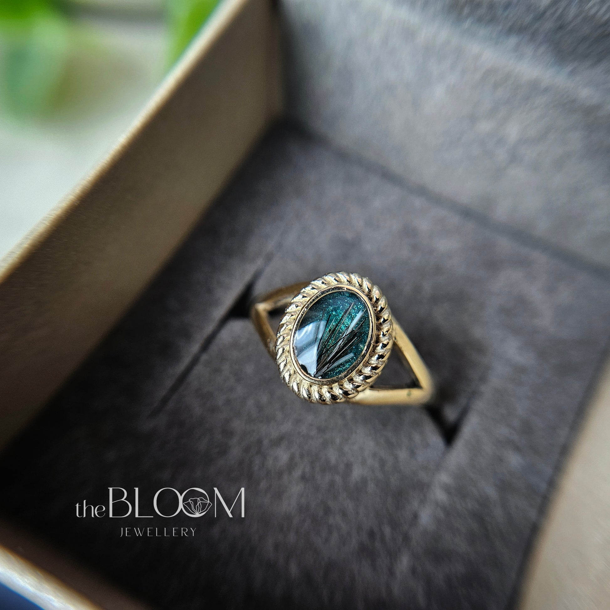 Gold ring with green stone in a box, branded 'the Bloom Jewellery'.
