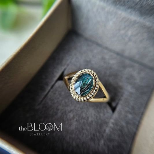 Gold ring with green stone in a box, branded 'the Bloom Jewellery'.