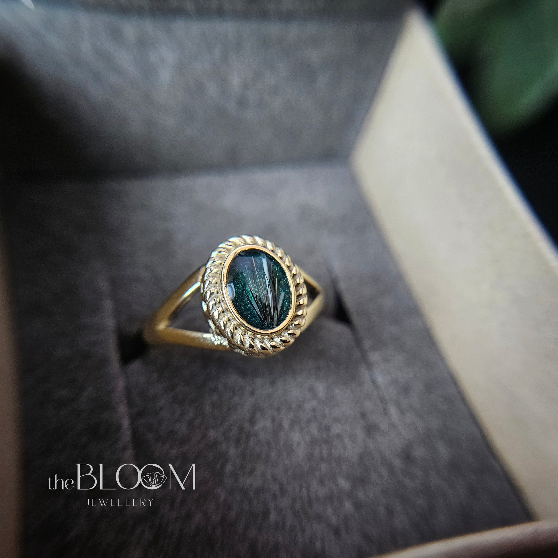 Gold ring with a green memorial stone in a box, branded 'the BLOOM JEWELLERY'.
