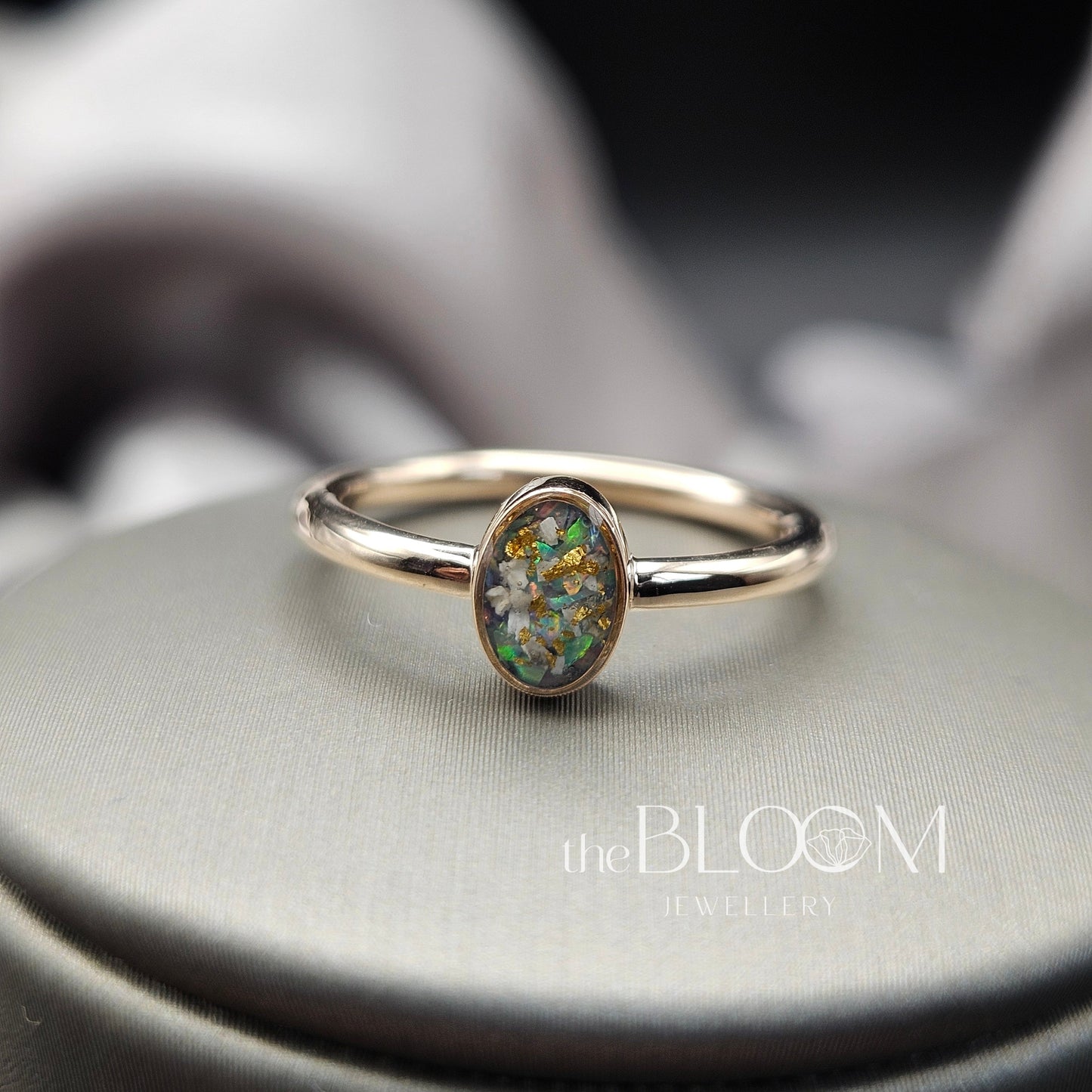 gold ring with a green gemstone on a gray surface, branded 'the BLOOM Jewellery'.