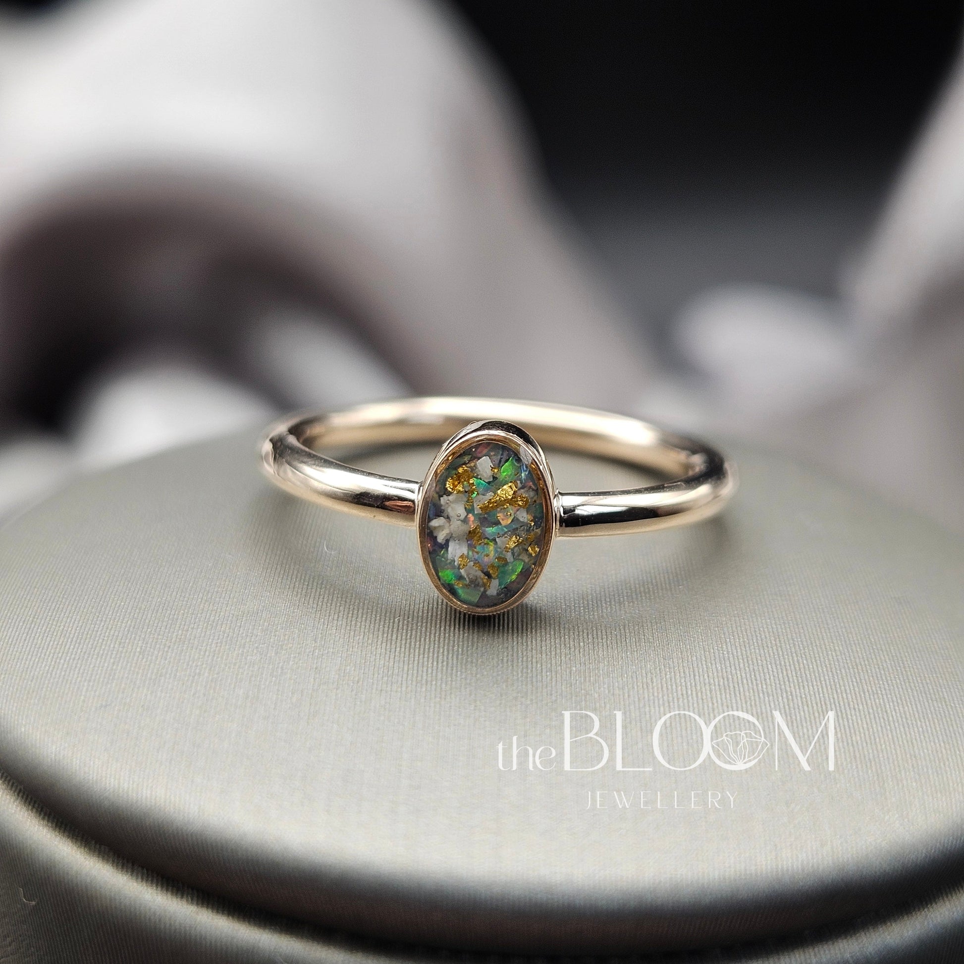 gold ring with a green gemstone on a gray surface, branded 'the BLOOM Jewellery'.