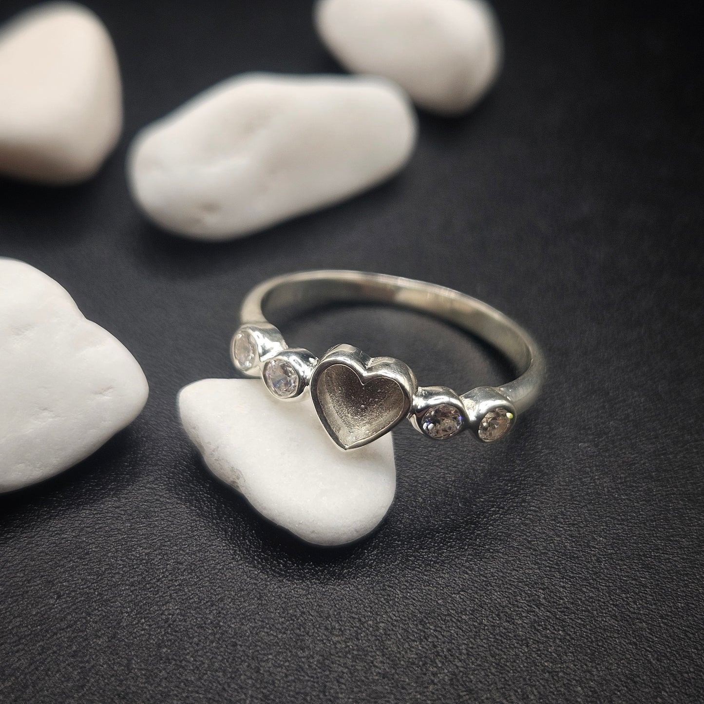 Silver ring with a heart design on a dark surface with white stones