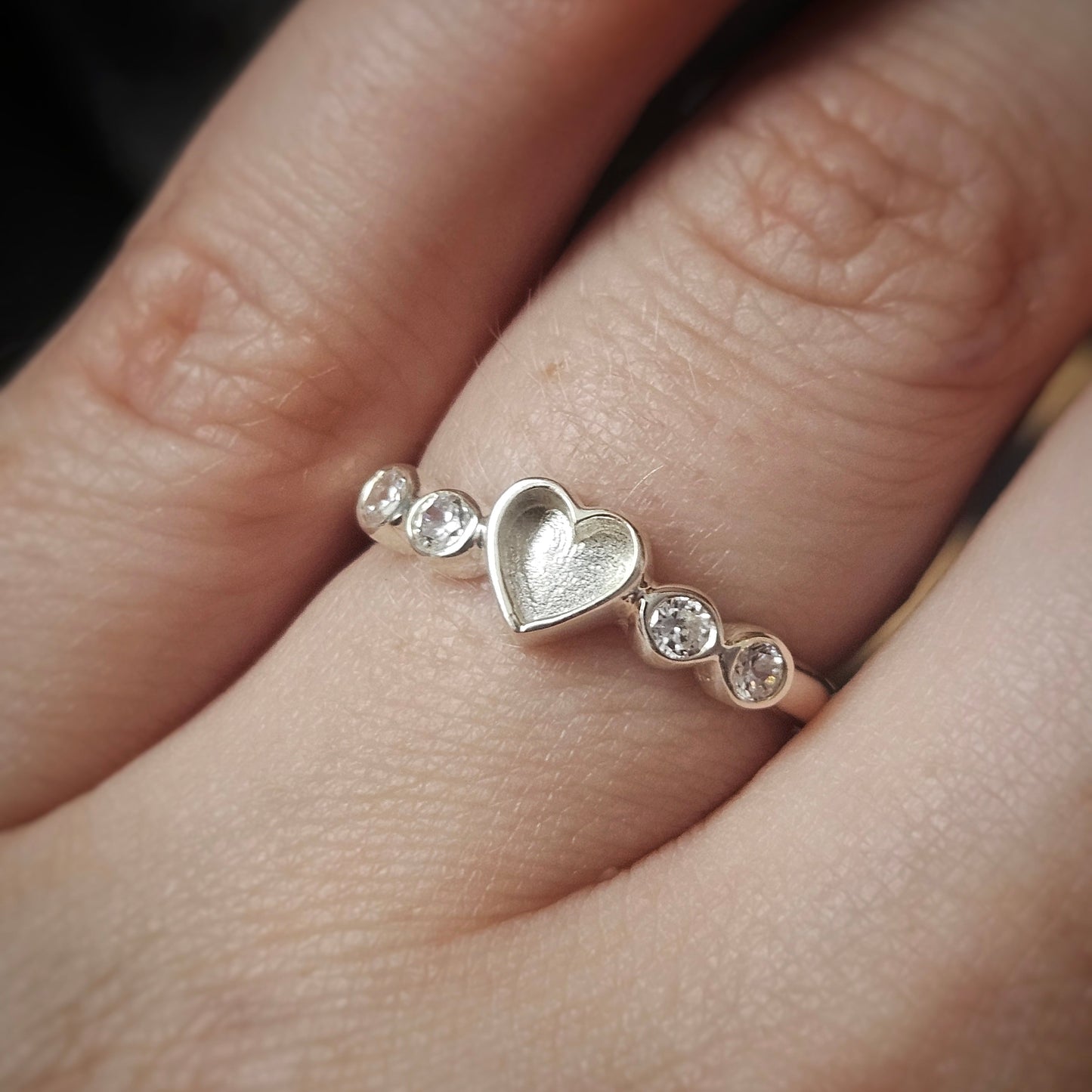 Silver heart-shaped ring with small diamonds on a finger